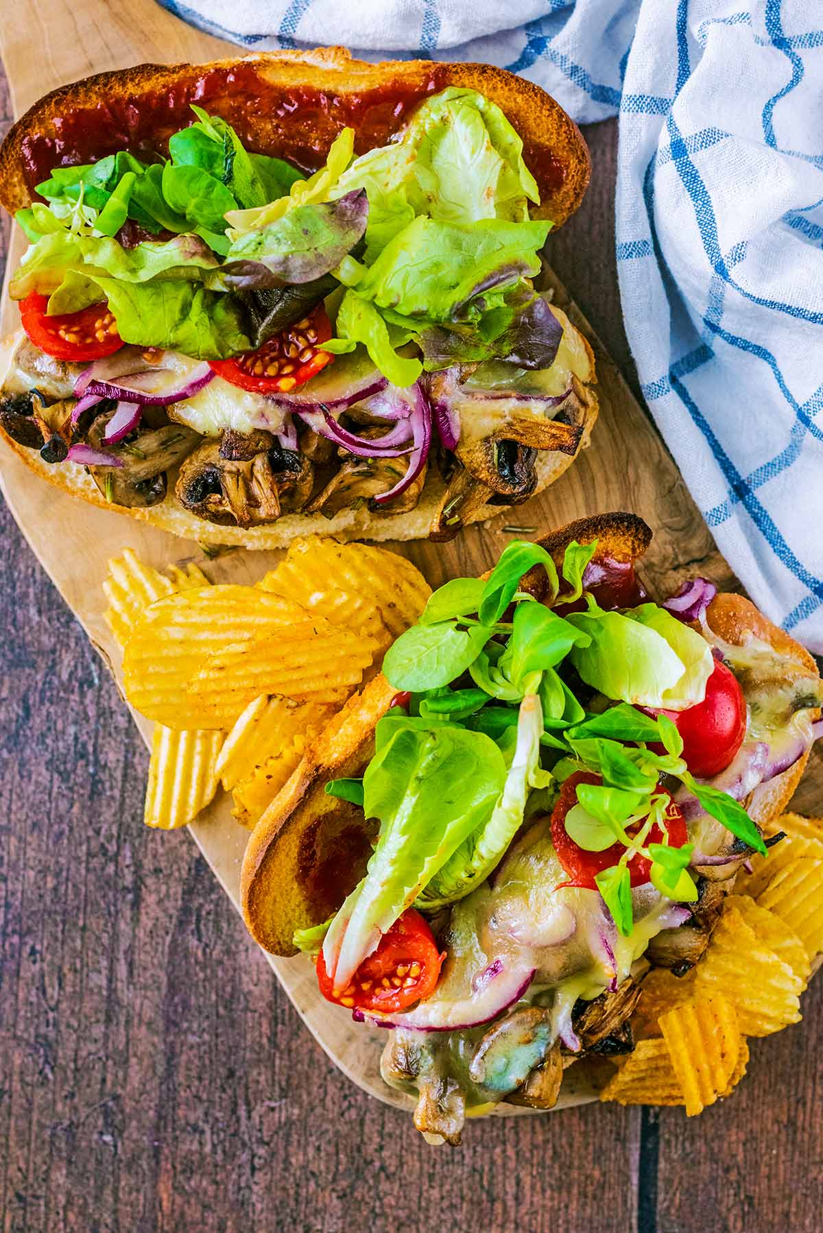 Two mushroom and salad sandwiches on a wooden serving board.