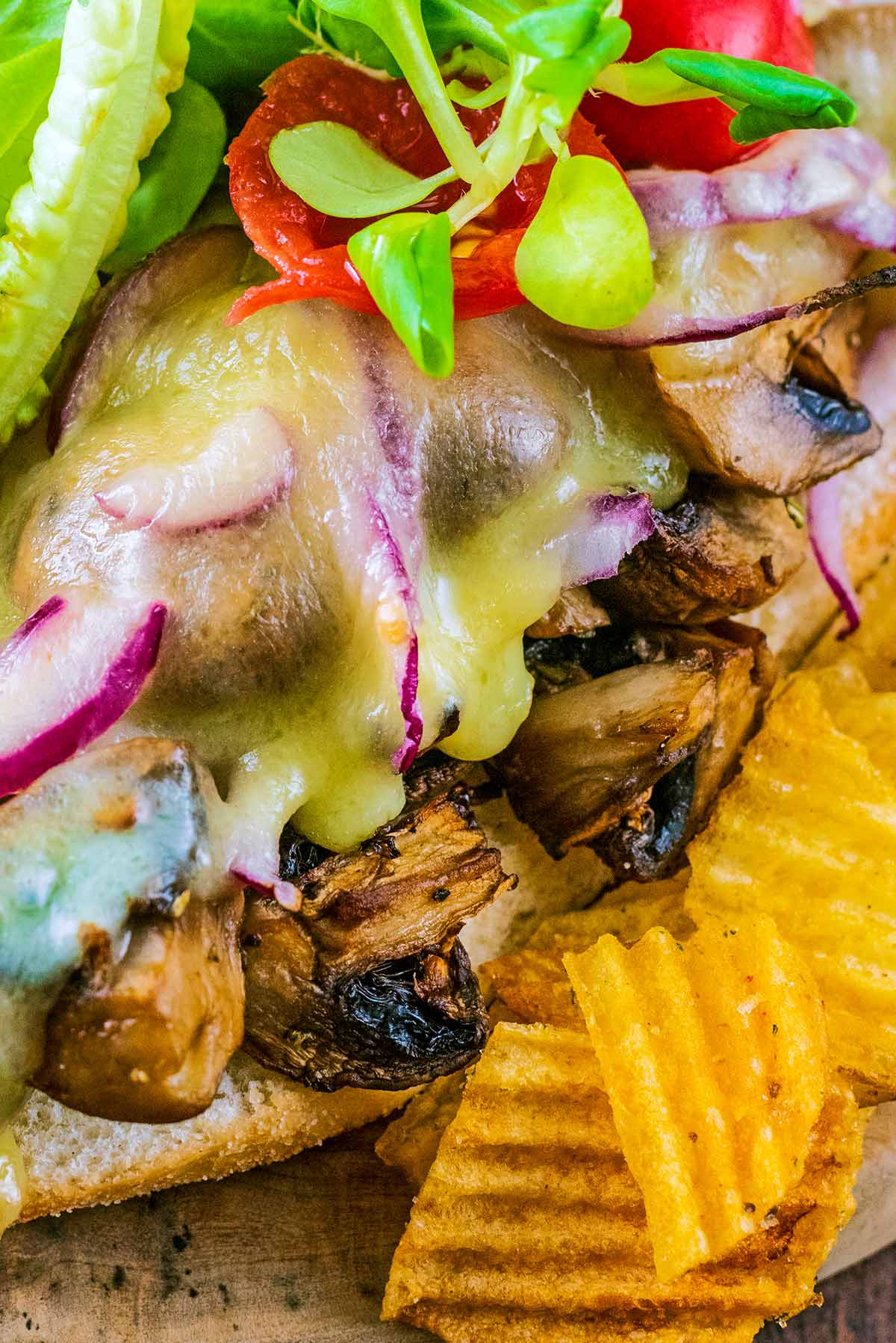Melted cheese dripping down some cooked mushrooms in a sandwich.