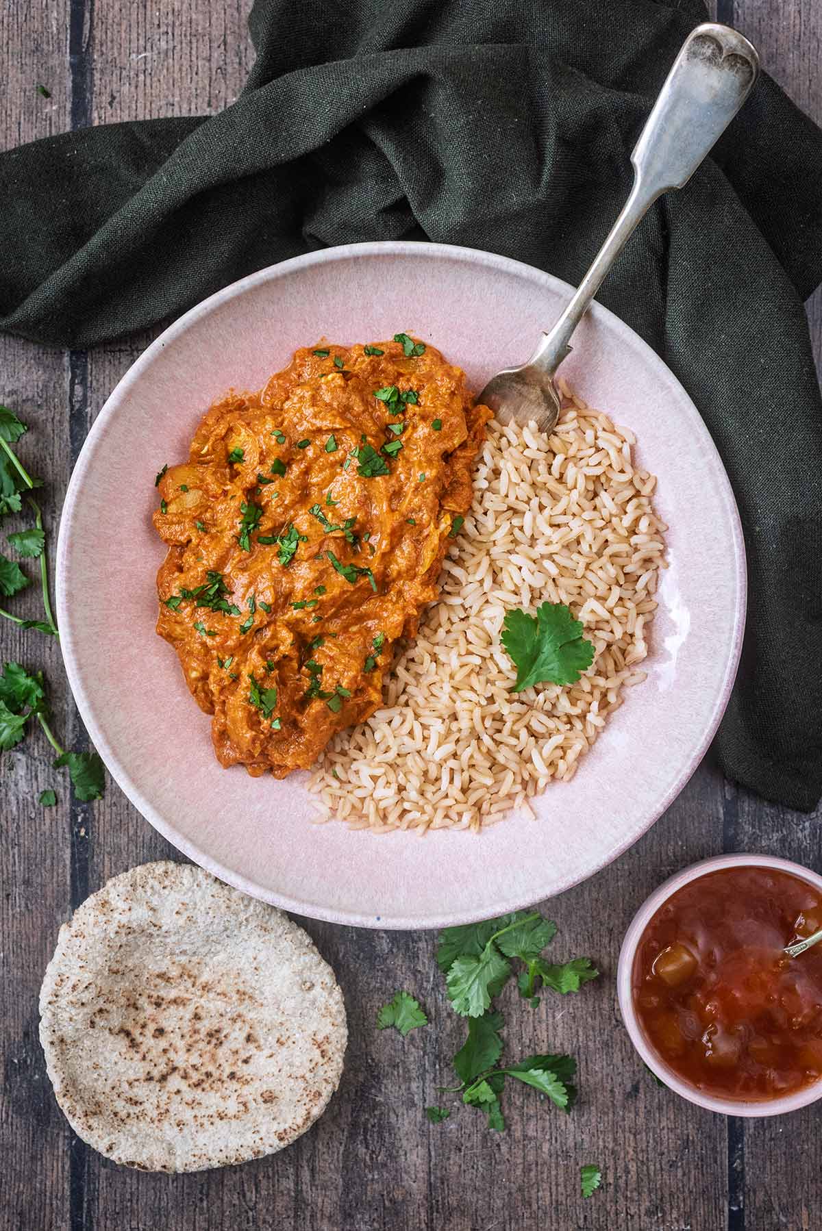 A bowl of chicken curry and rice next to a naan bread and bowl of mango chutney.