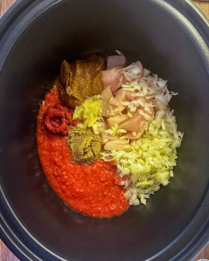 Chicken, onions, tomatoes, curry paste and spices in a slow cooker bowl.