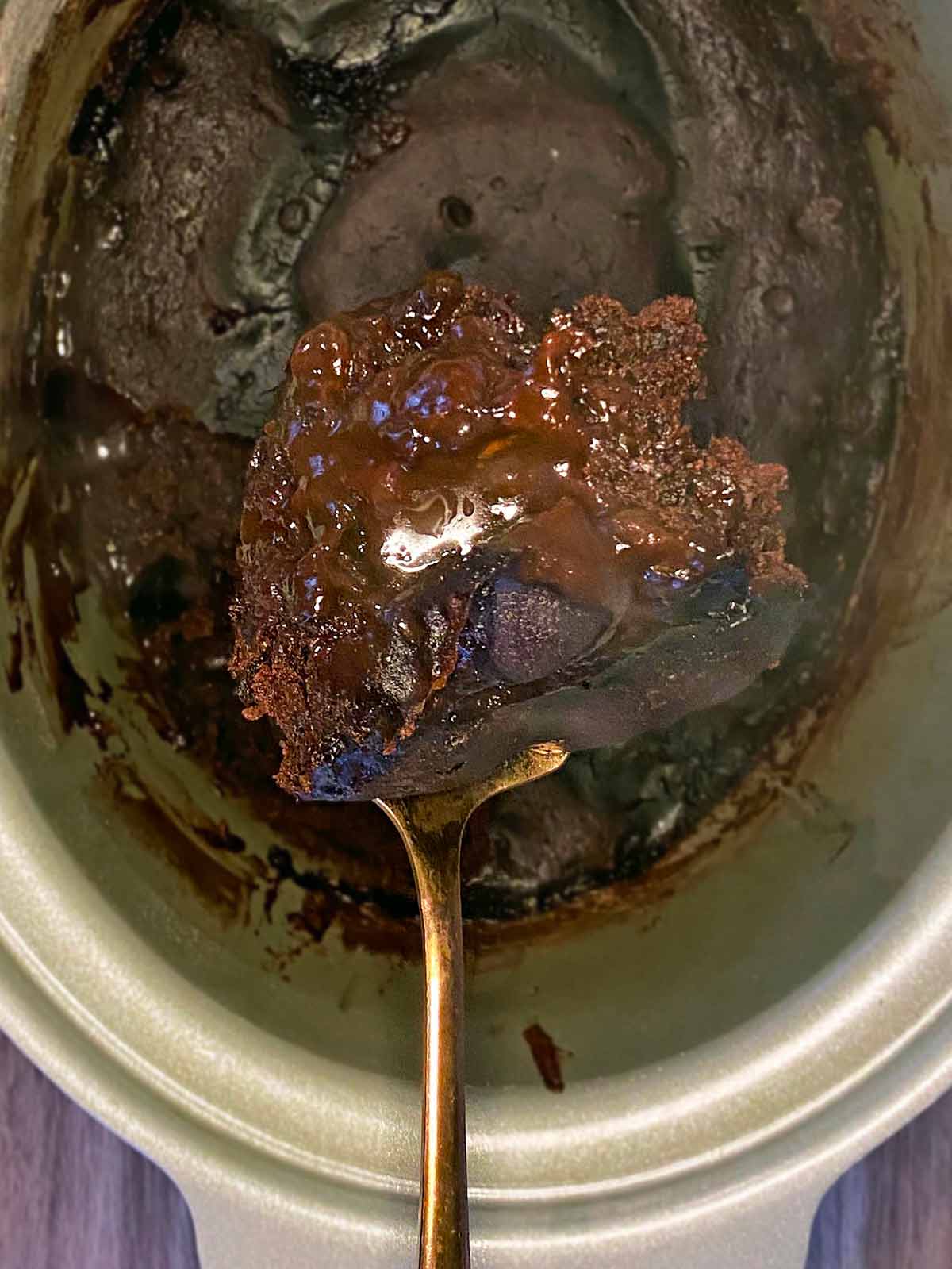 A spoon lifting out some cake from the slow cooker.