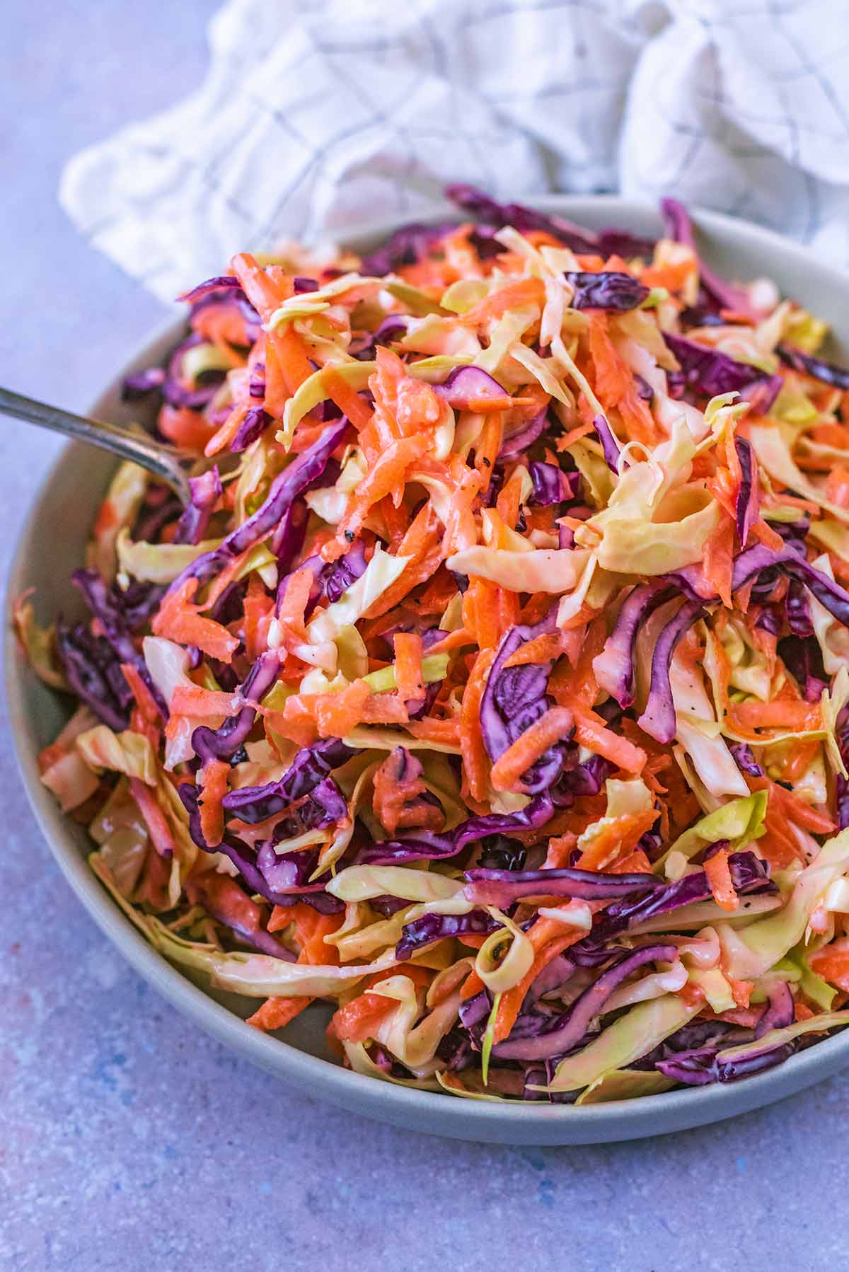 A fork lifting some coleslaw from a bowl.
