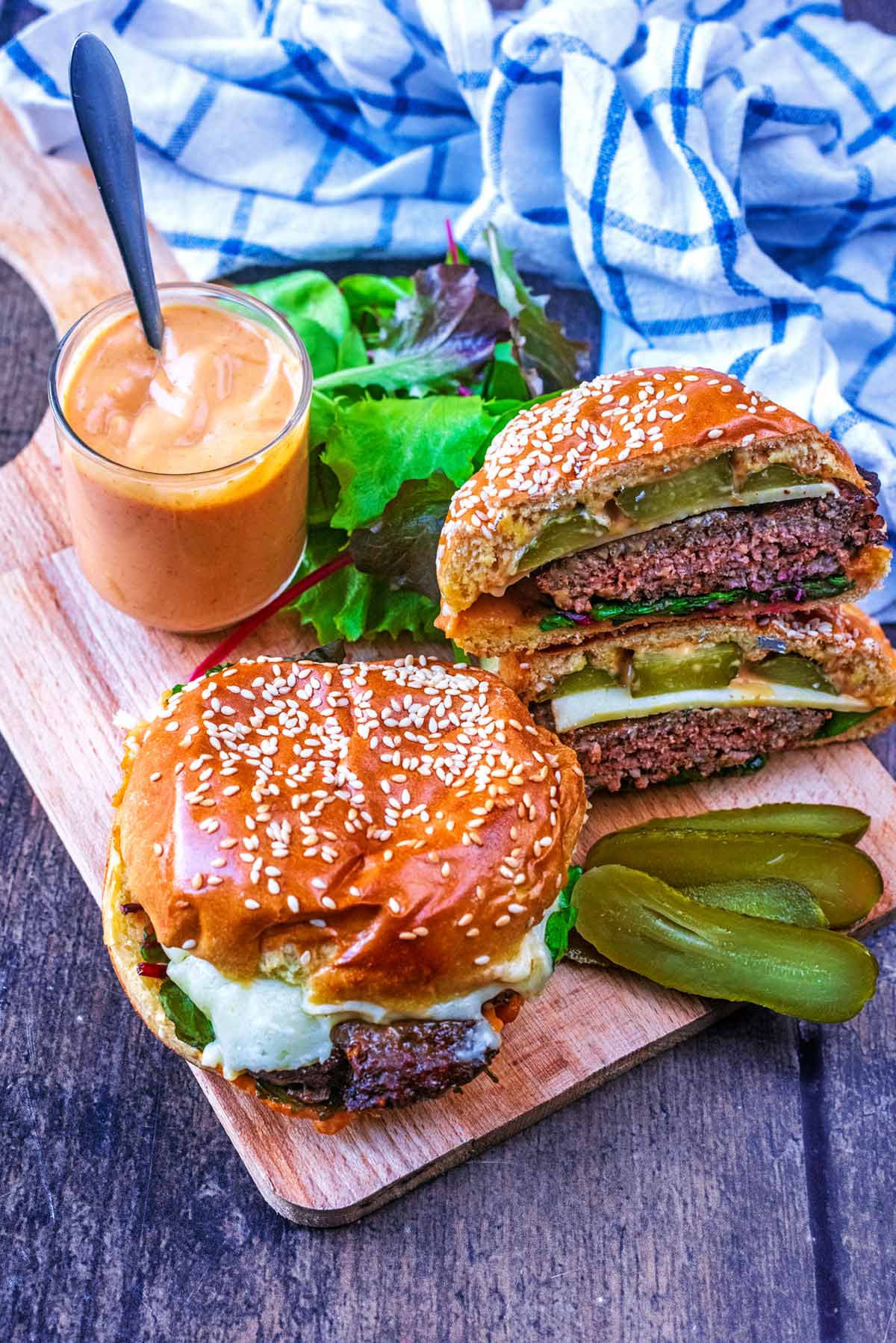 Two hamburgers on a wooden board, one is cut in half.