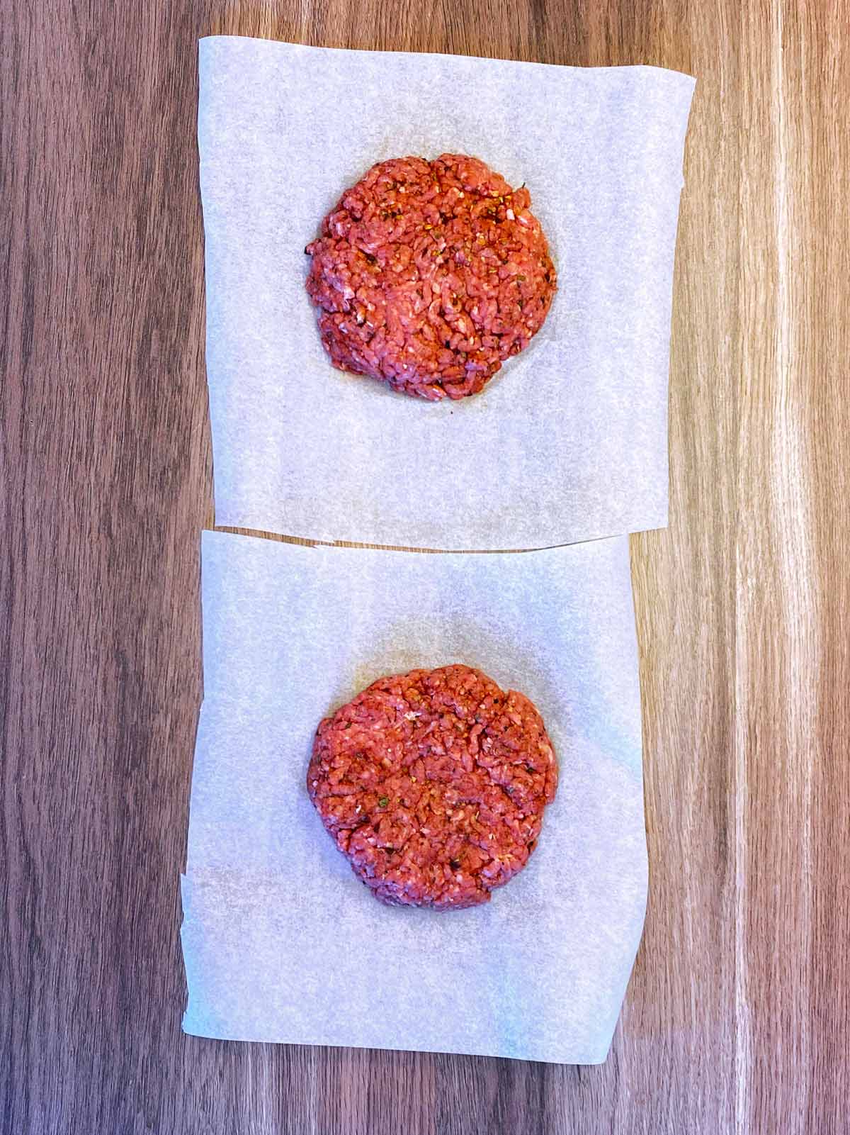 Two raw burger patties on parchment paper.