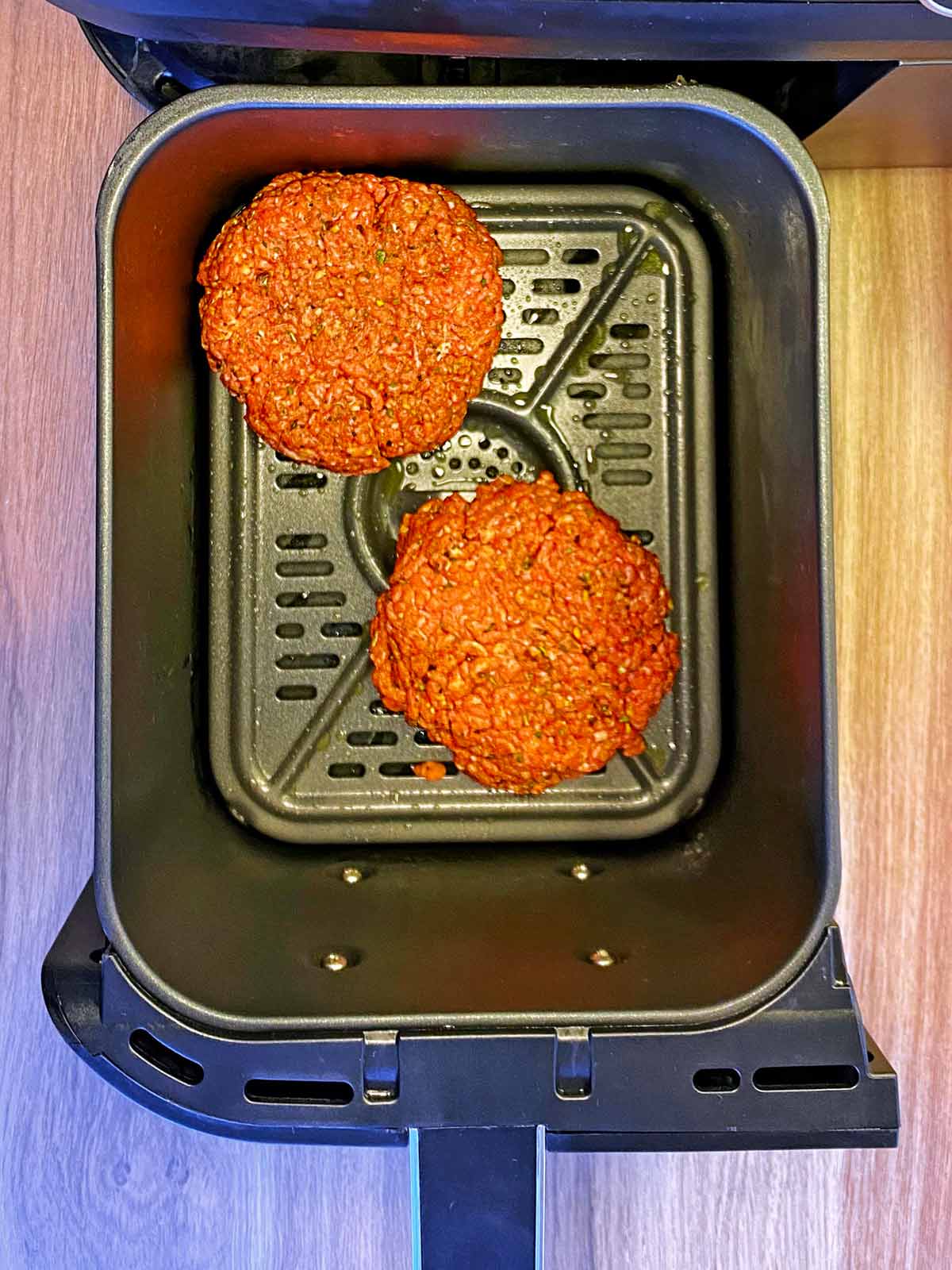 Two uncooked burger patties in an air fryer basket.