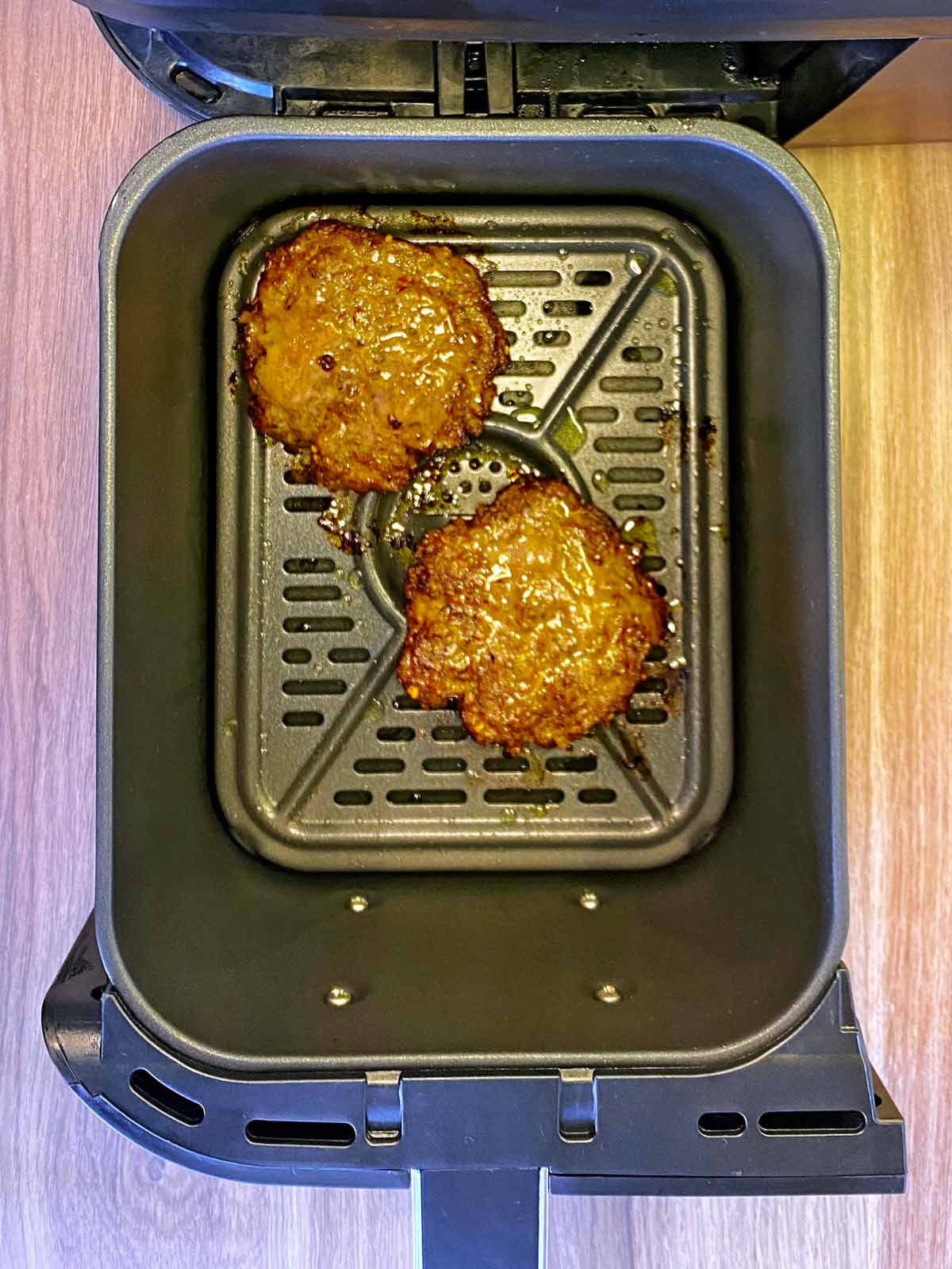 Cooked burgers in an air fryer basket.