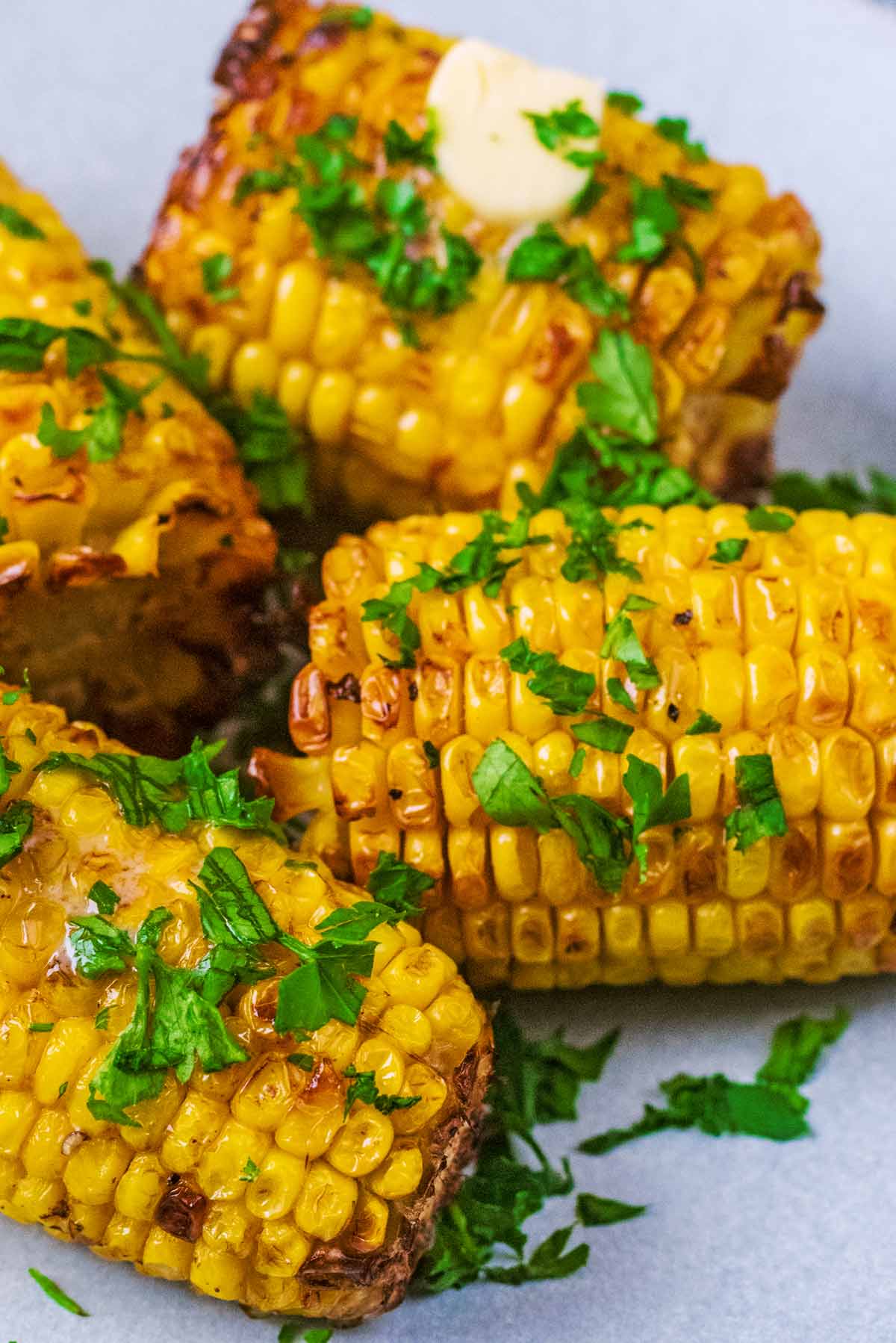 Four cooked corn cobs topped with butter and chopped herbs.