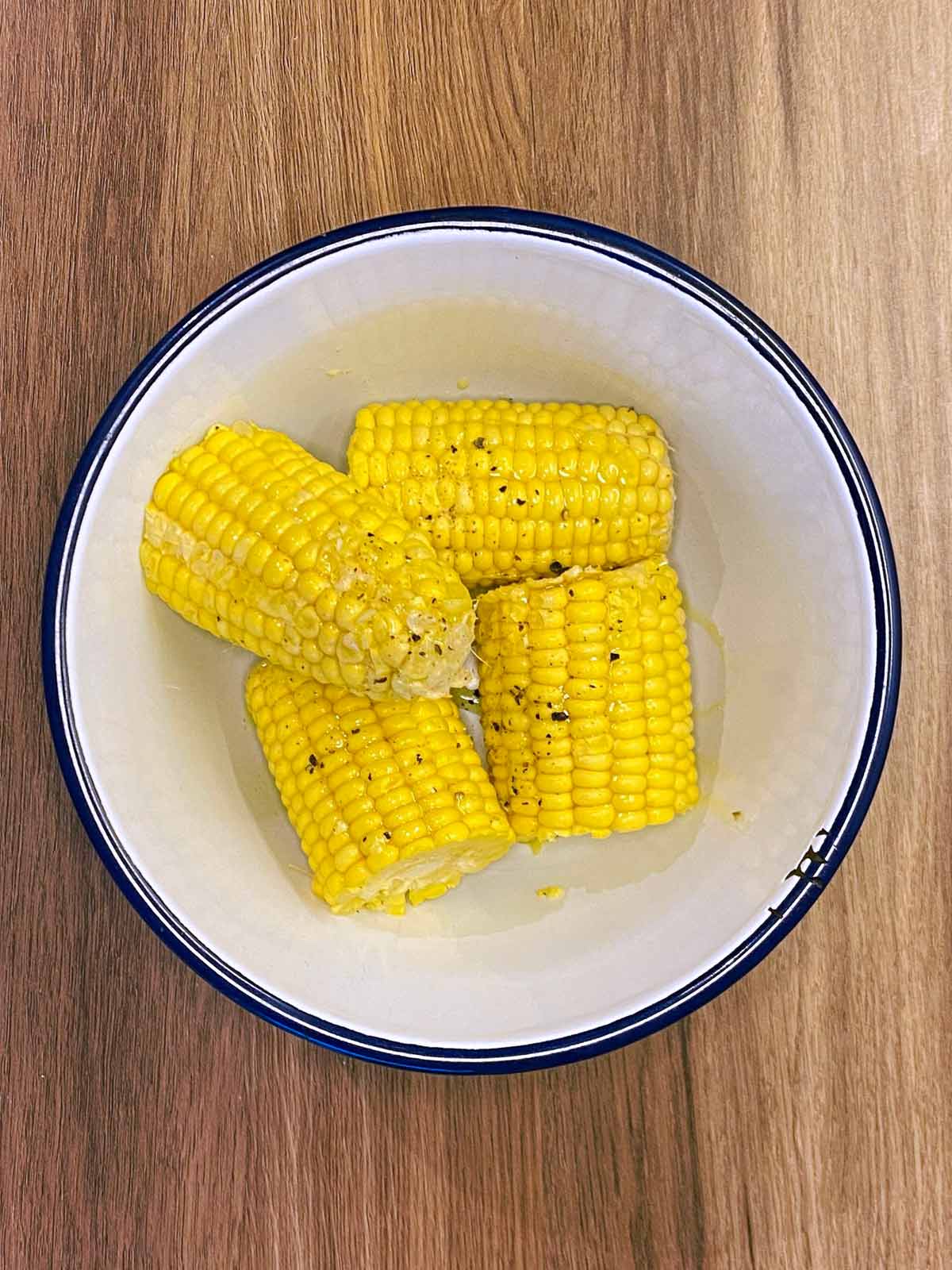 Four corn cobs in a bowl covered in oil and seasoning.
