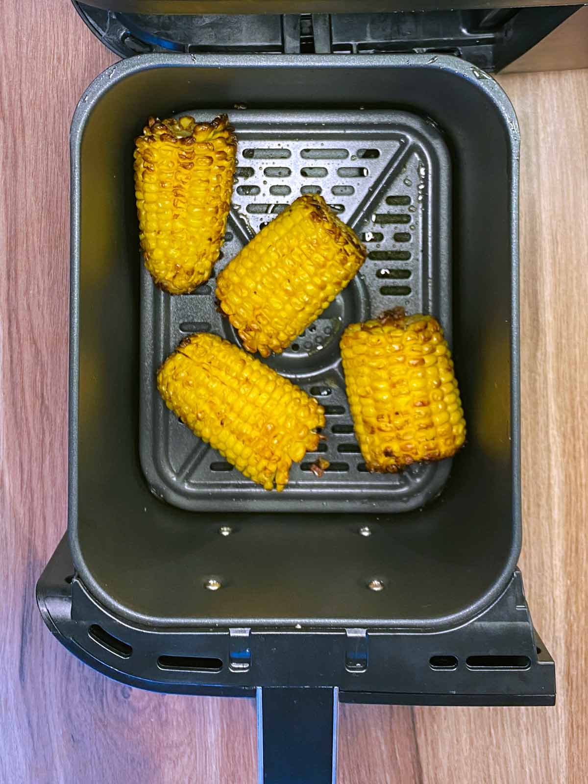 Four cooked corn cobs in an air fryer basket.