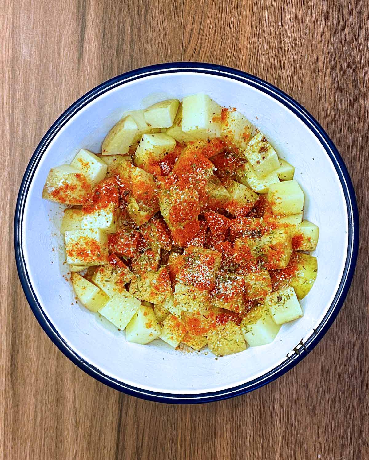 Uncooked diced potatoes in a bowl with herbs and spices on them.