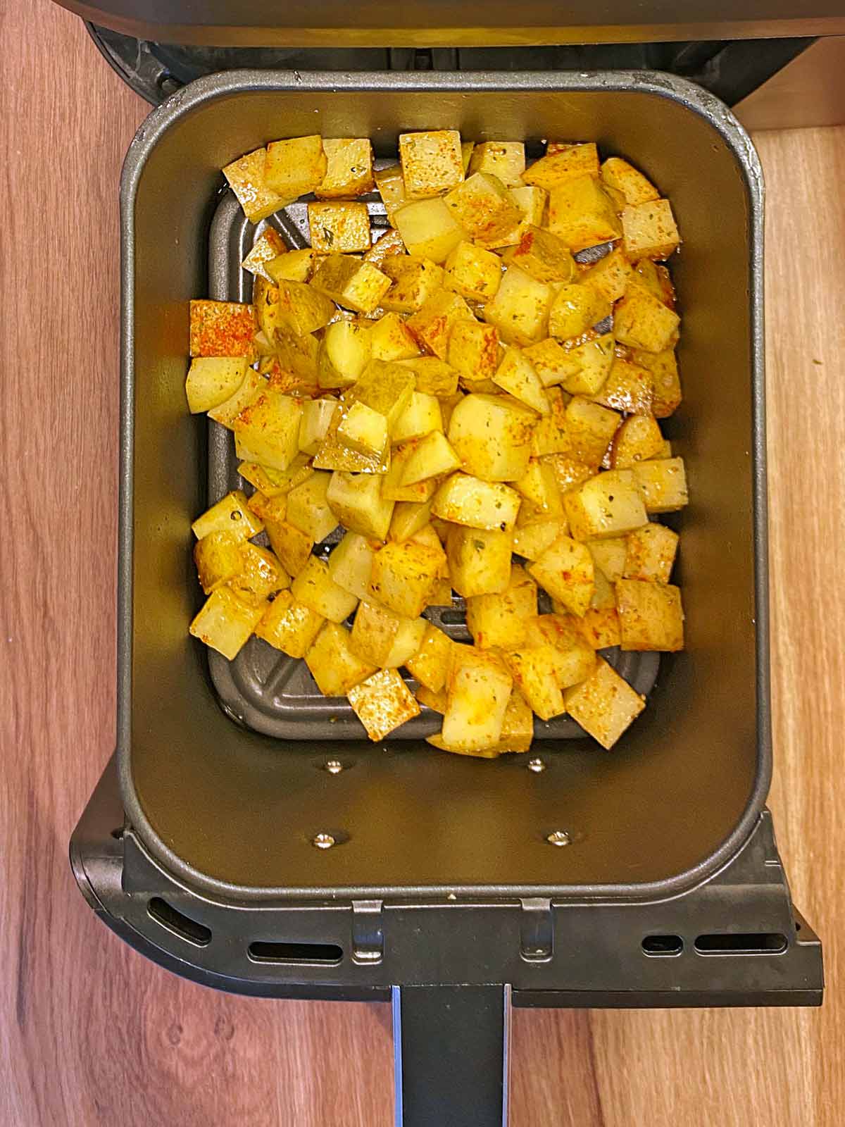 Cubes of seasoned potato in n air fryer basket.