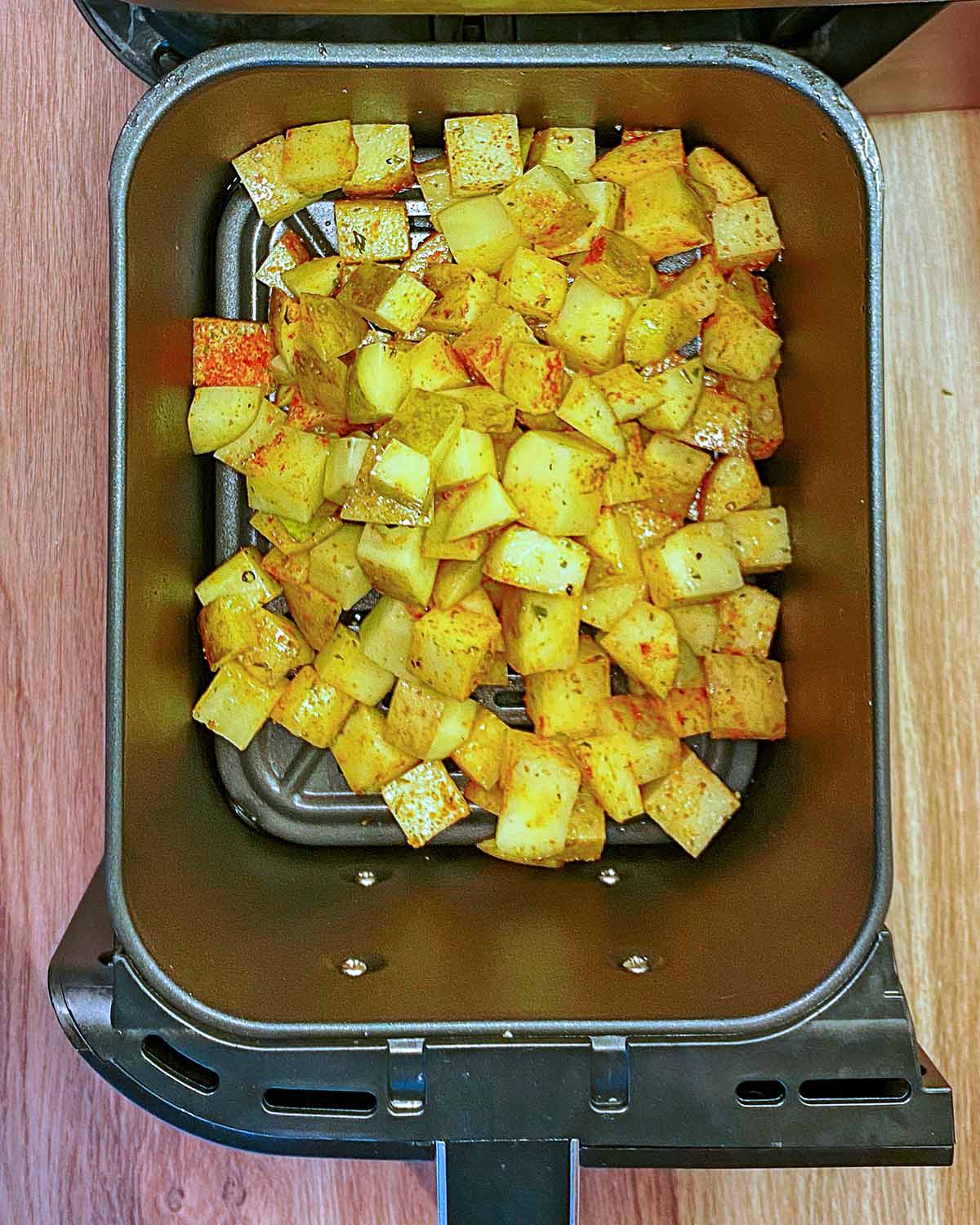 Cubes of seasoned potato in an air fryer basket.