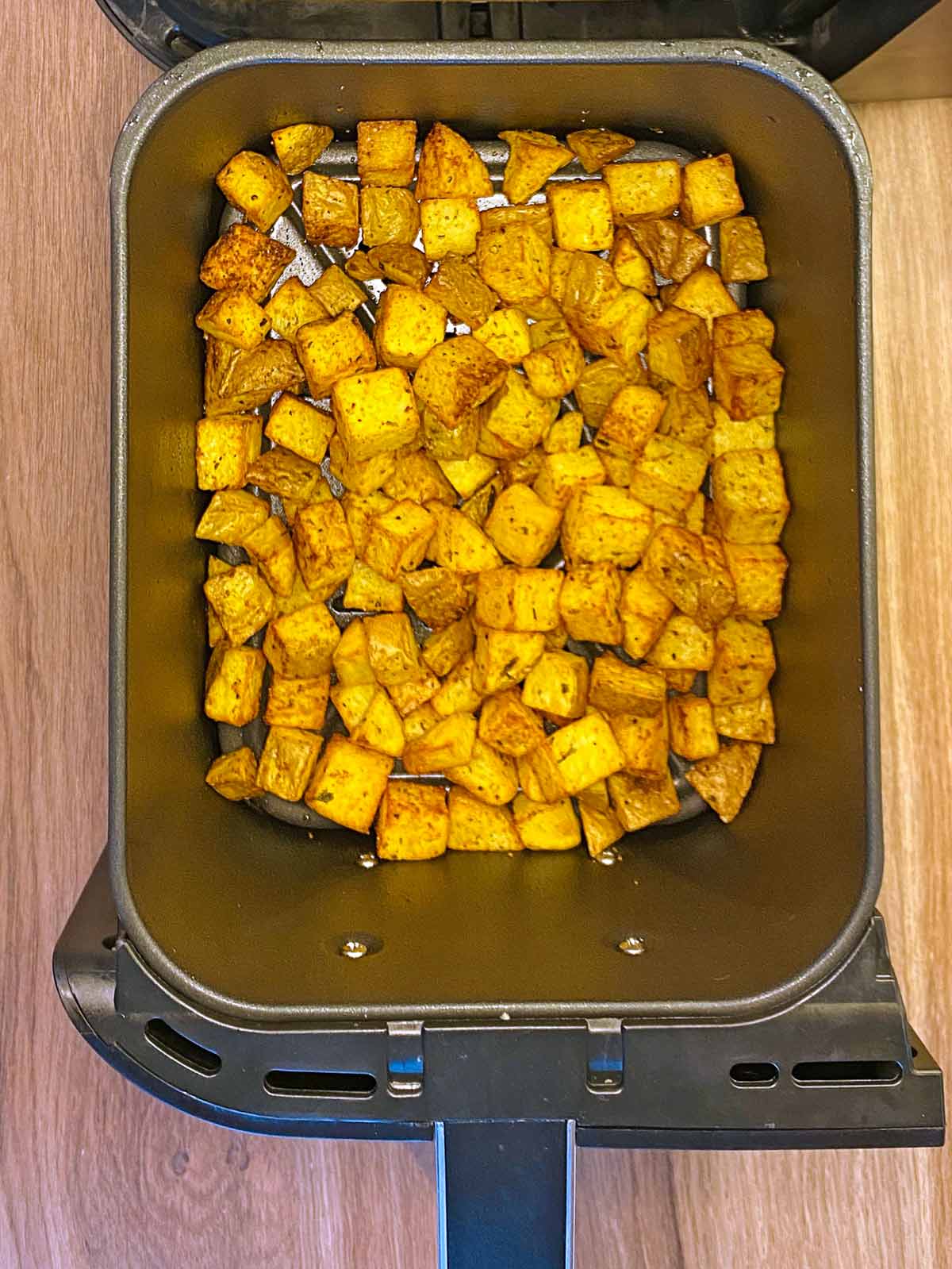 Cooked potato cubes in an air fryer.