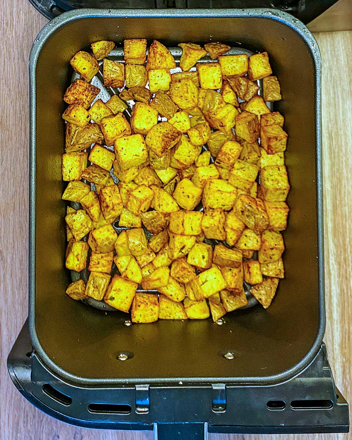 Cooked potato cubes in an air fryer.