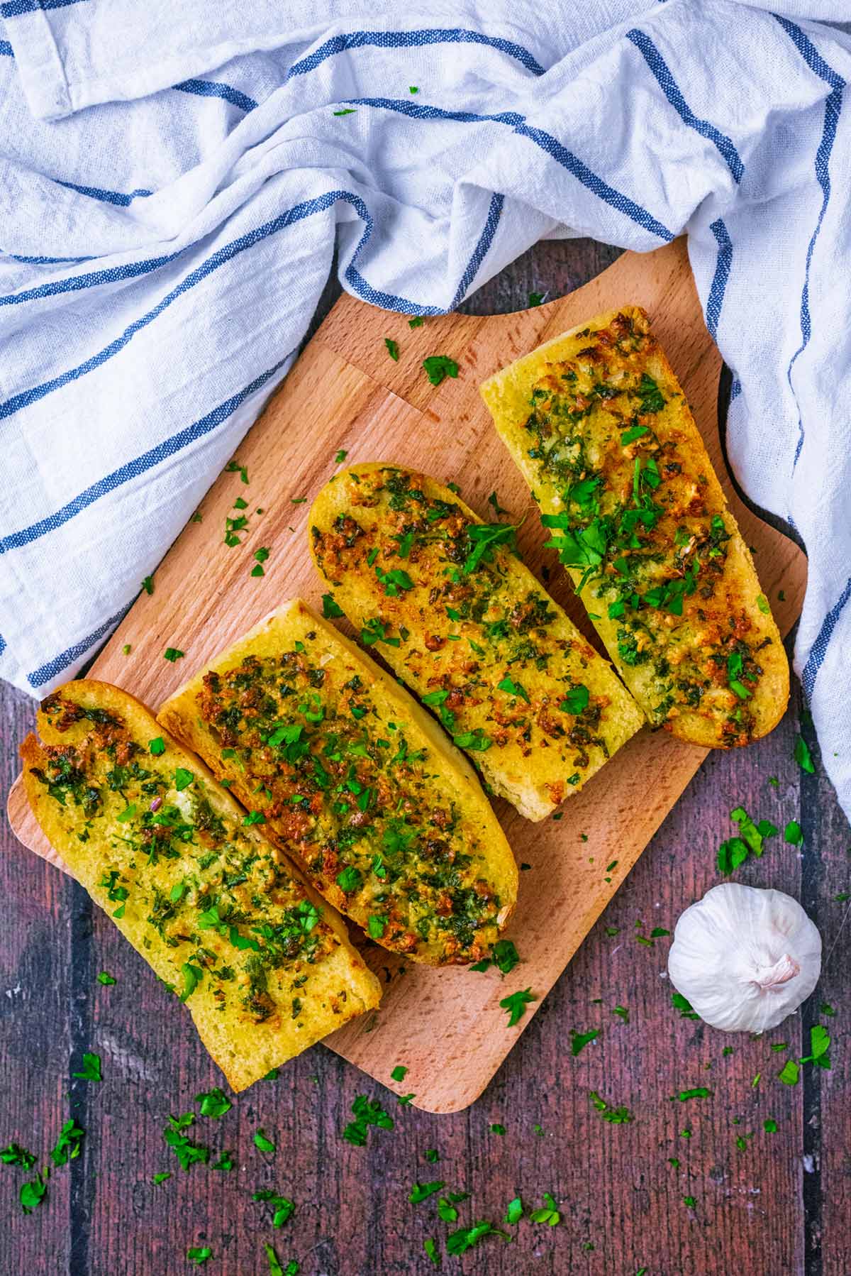 Four slices of garlic bread on a board topped next to a bulb of garlic.