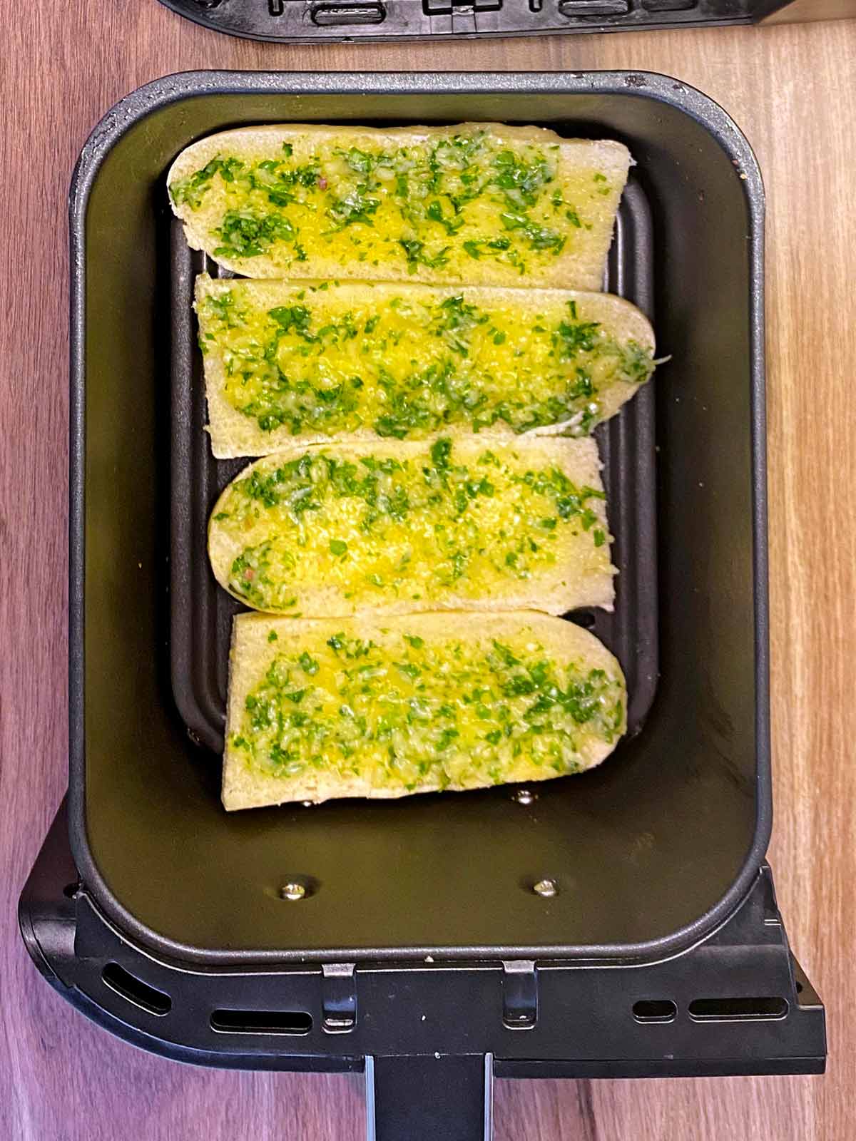 Four slices of uncooked garlic bread in an air fryer basket.