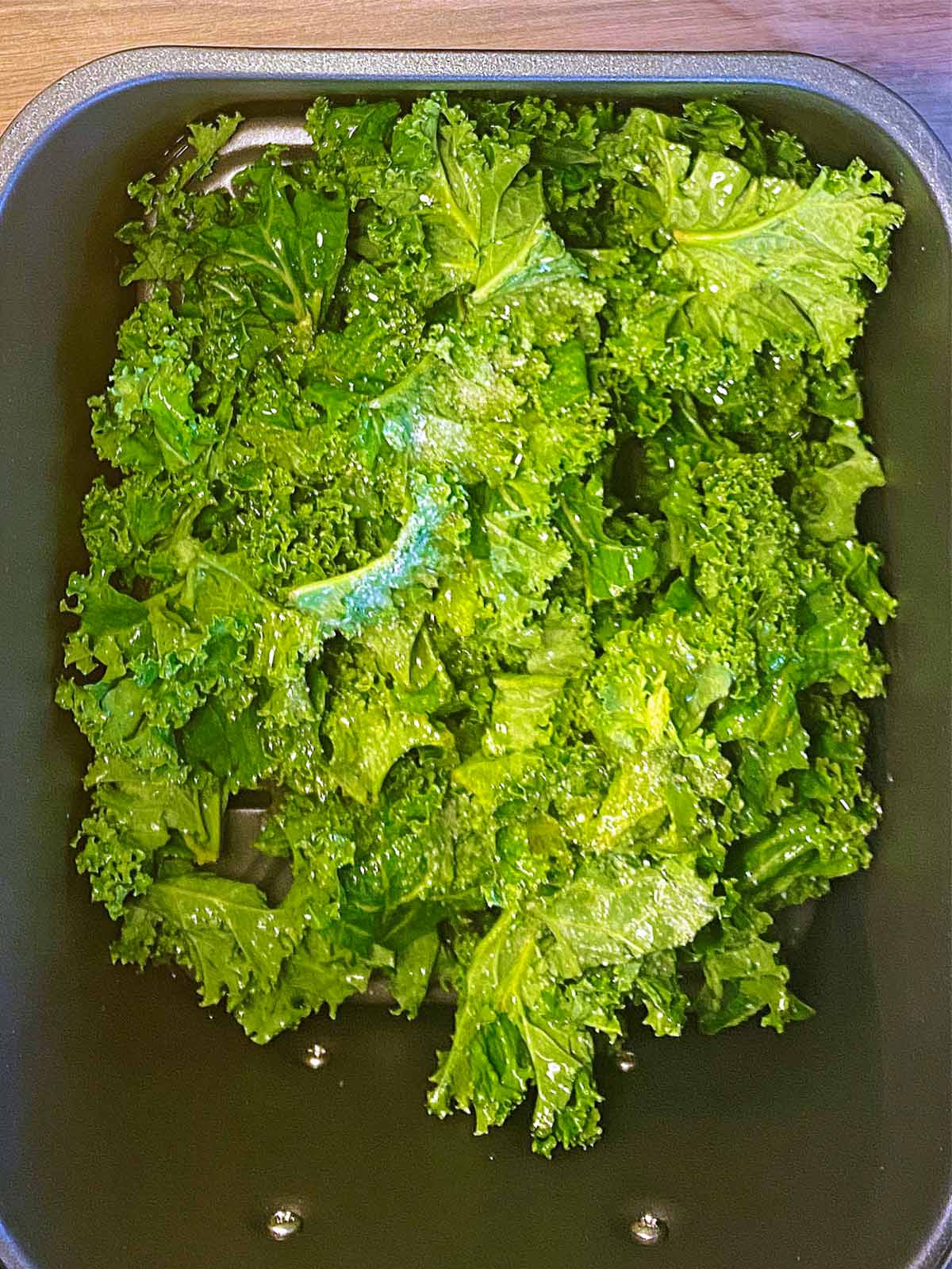 An air fryer basket full of kale leaves.