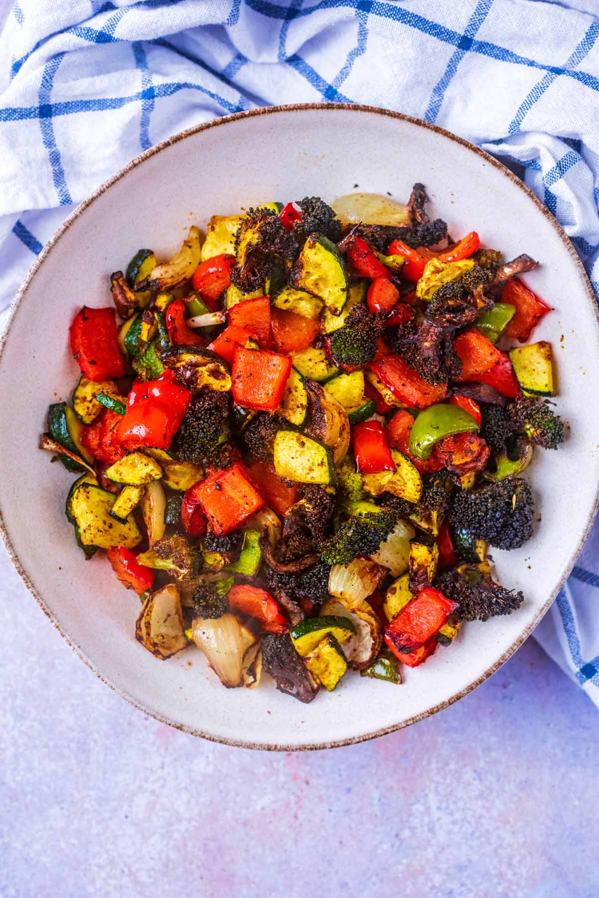 A bowl full of roasted vegetables next to a checked towel.