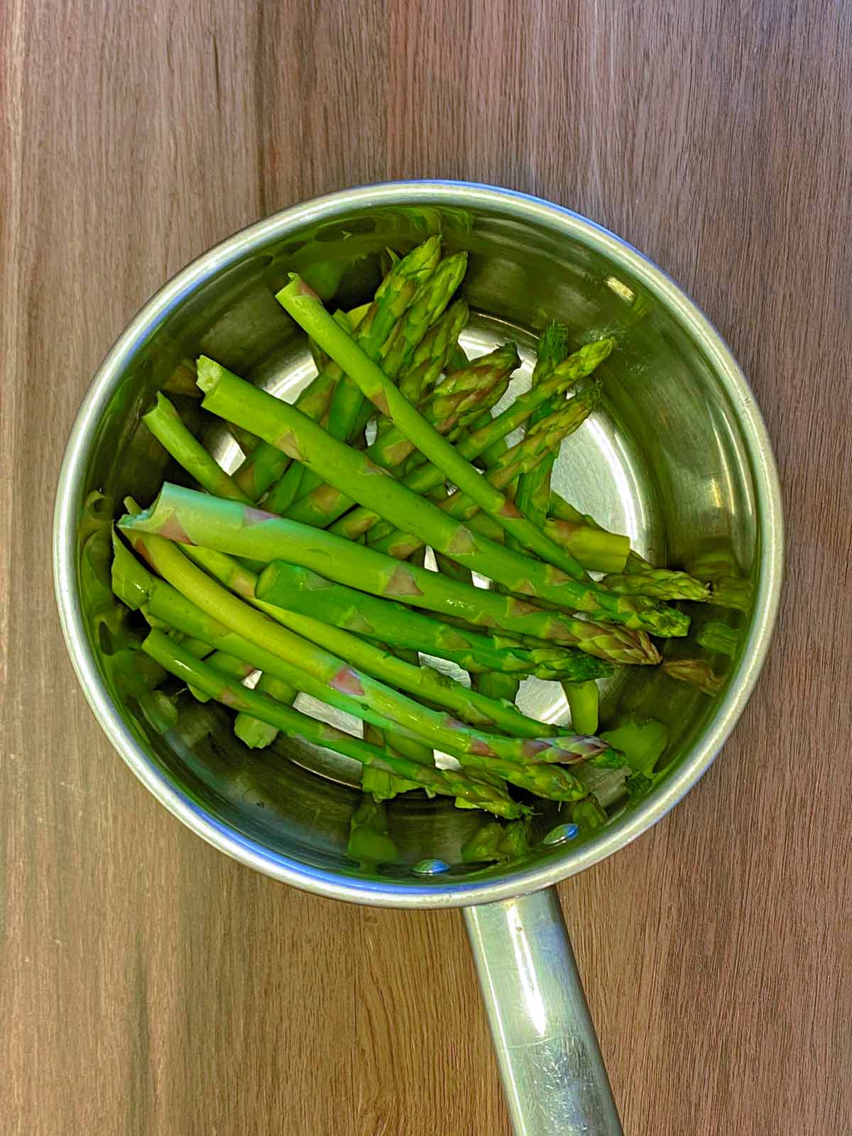 A saucepan with raw asparagus spears in it.