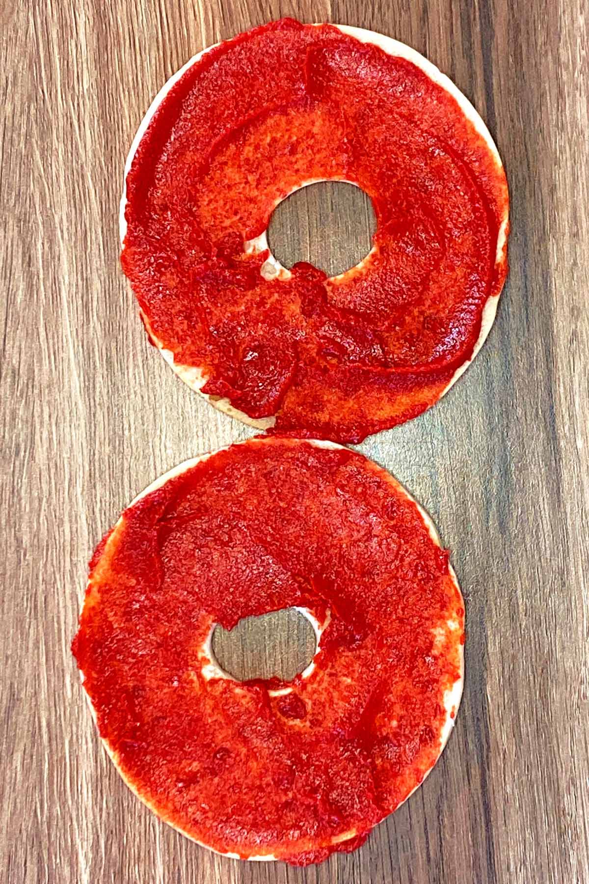 Two bagel halves with tomato puree spread on them.