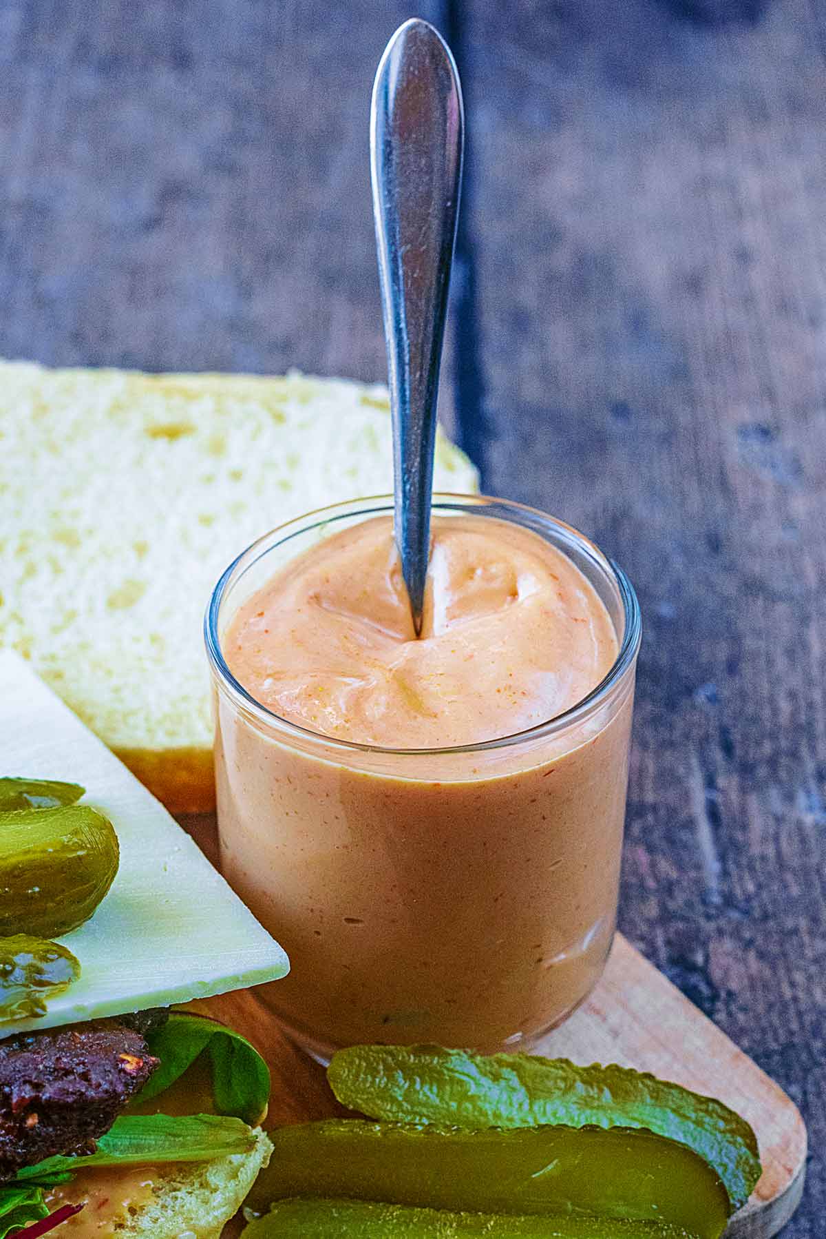 A glass full of burger sauce with a spoon in it.
