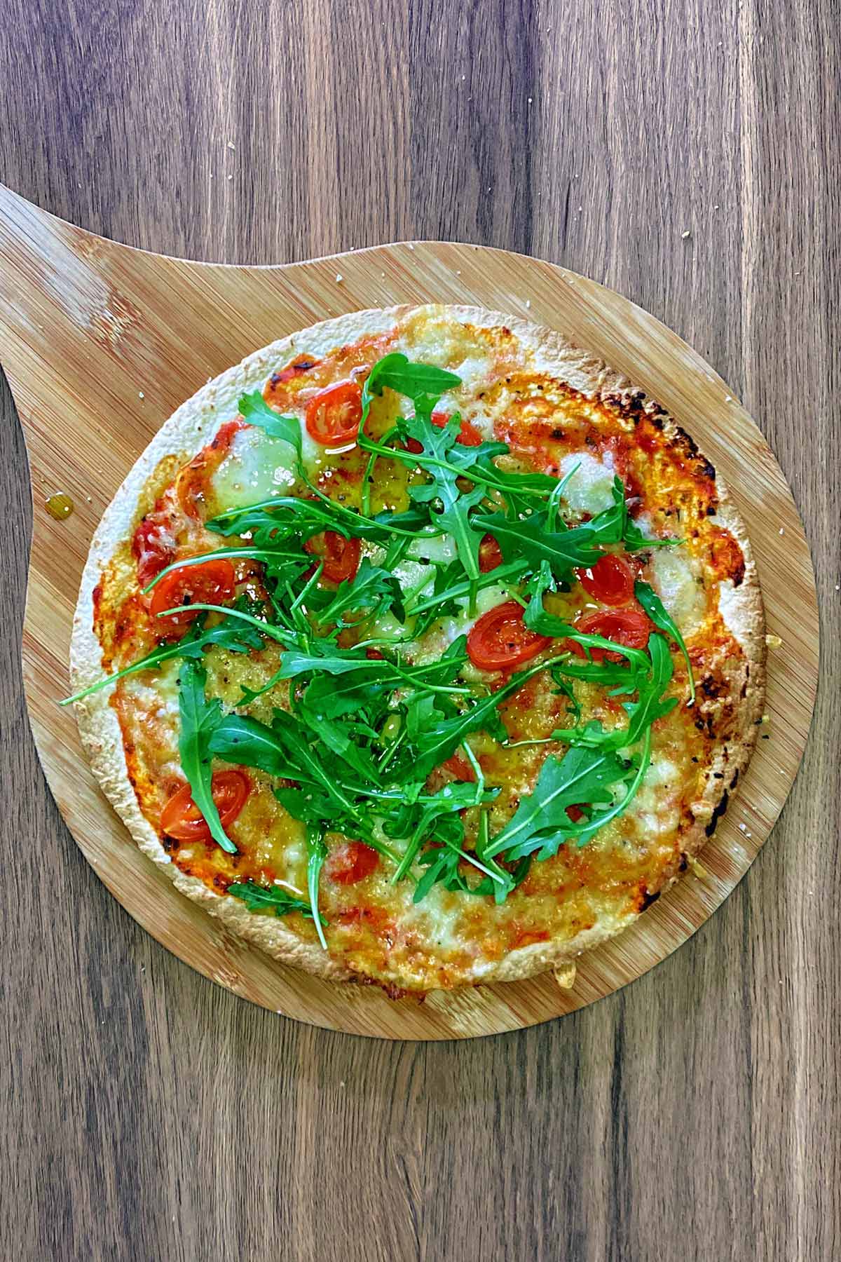 A pizza topped with rocket leaves on a wooden board.