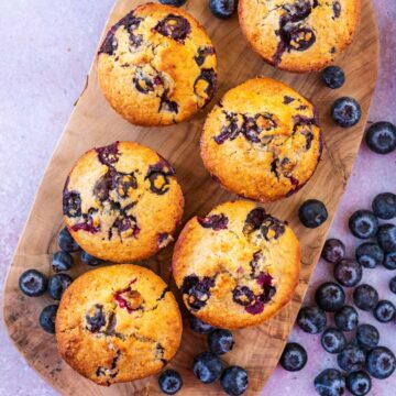 Six healthy blueberry muffins on a wooden serving board.