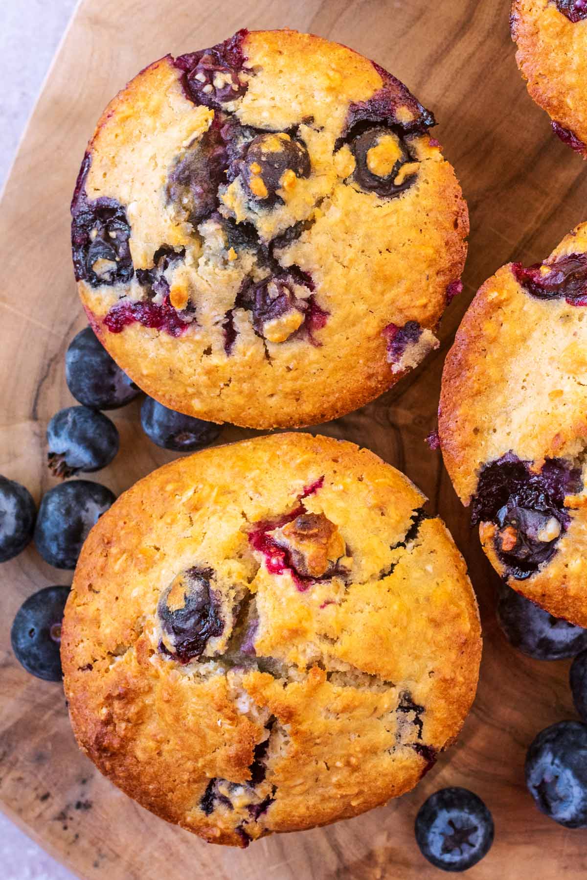 Two blueberry muffins surrounded by some blueberries.