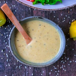 Tahini dressing in a small bowl with a small wooden spoon.