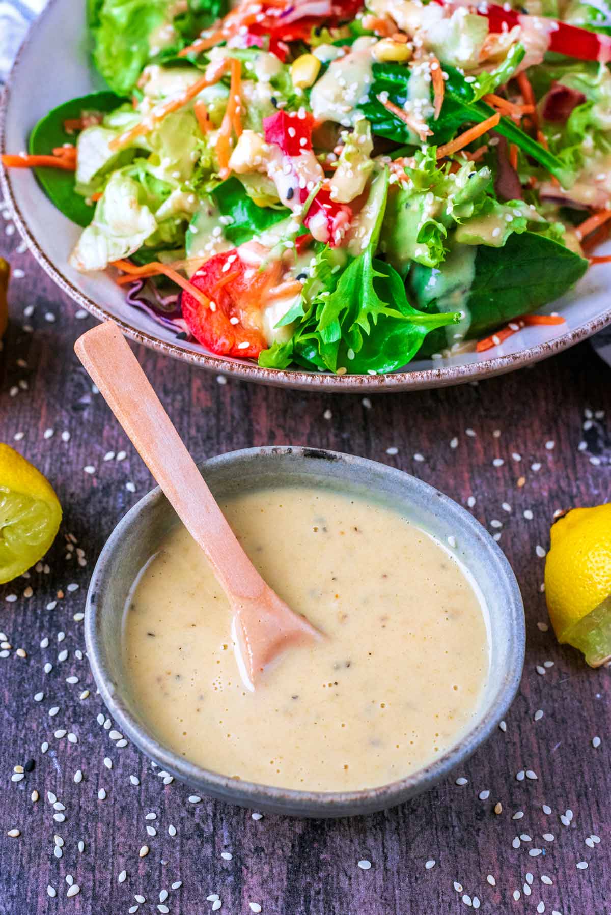 A bowl of tahini dressing in front of a bowl of salad.