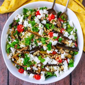 A large bowl of aubergine salad next to a yellow towel.