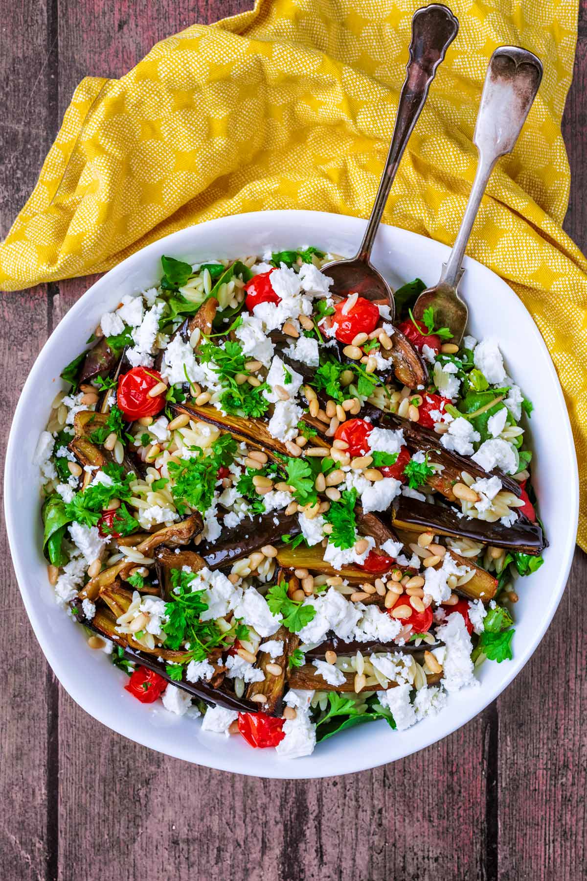 A bowl of salad topped with aubergines, tomatoes and crumbled feta cheese.