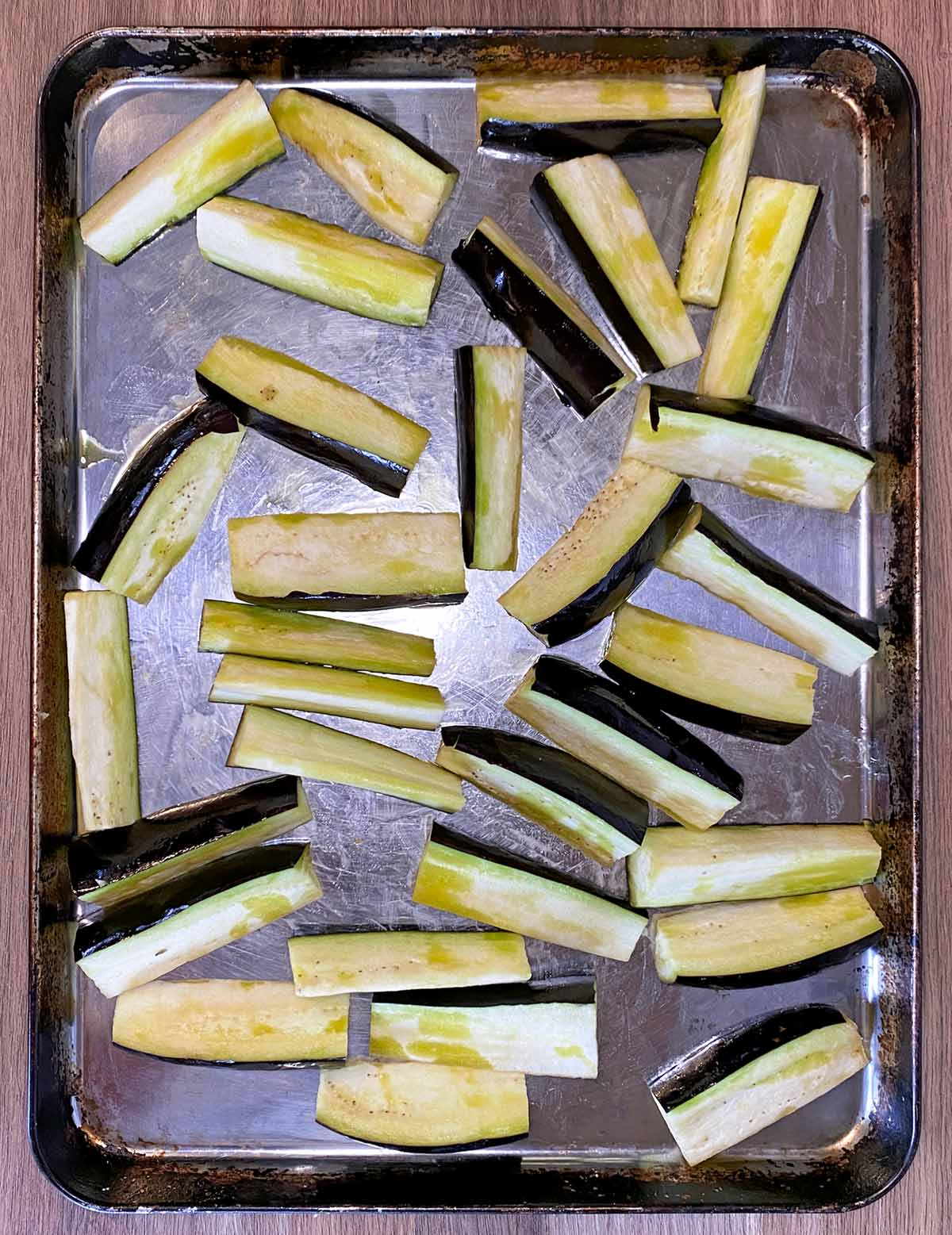 Wedges of aubergine drizzled with oil on a baking tray.