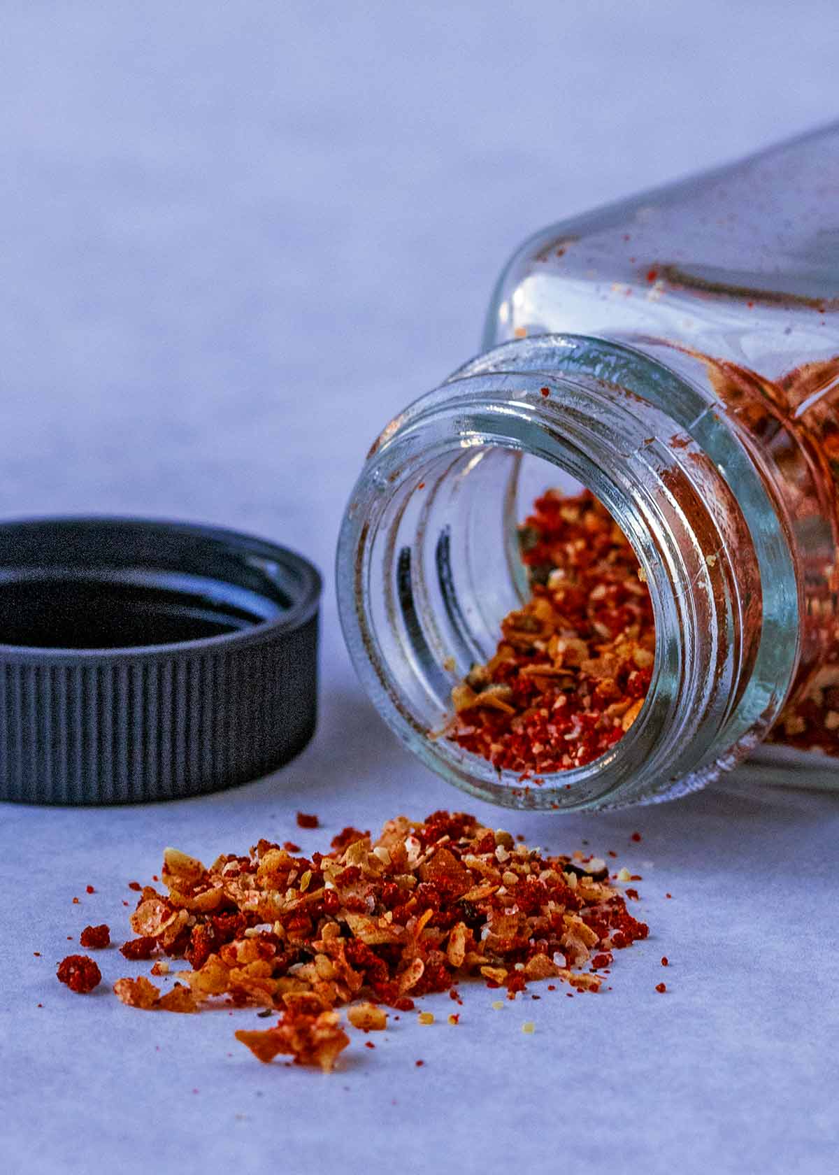 A glass jar, laying down, with a red coloured spice blend spilling out.
