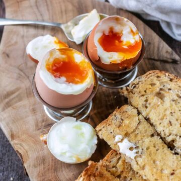 Two dippy eggs with soldiers on a wooden serving board.