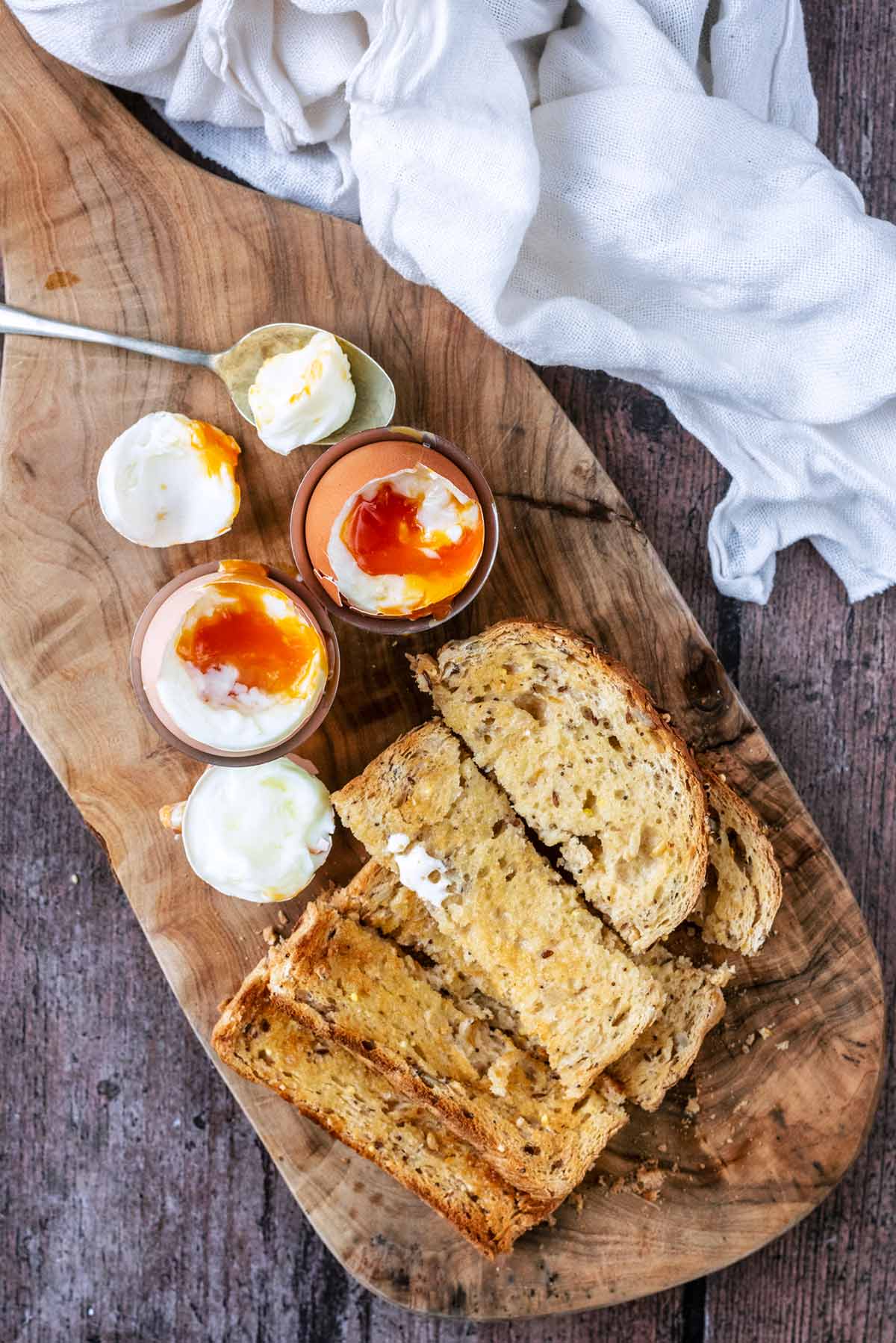 Two soft boiled eggs and toast soldiers on a wooden serving board.