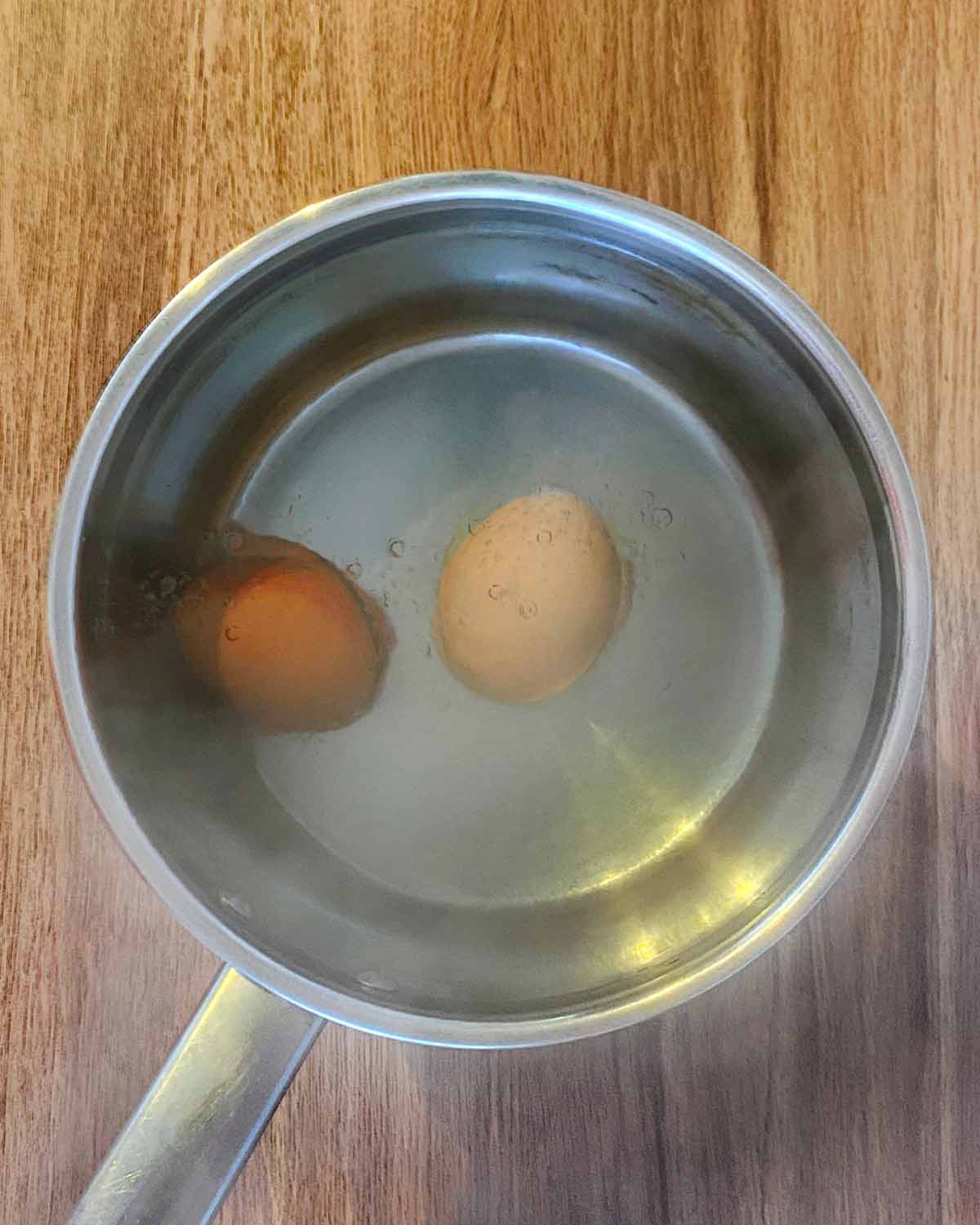 Two whole eggs in a pan of boiling water.