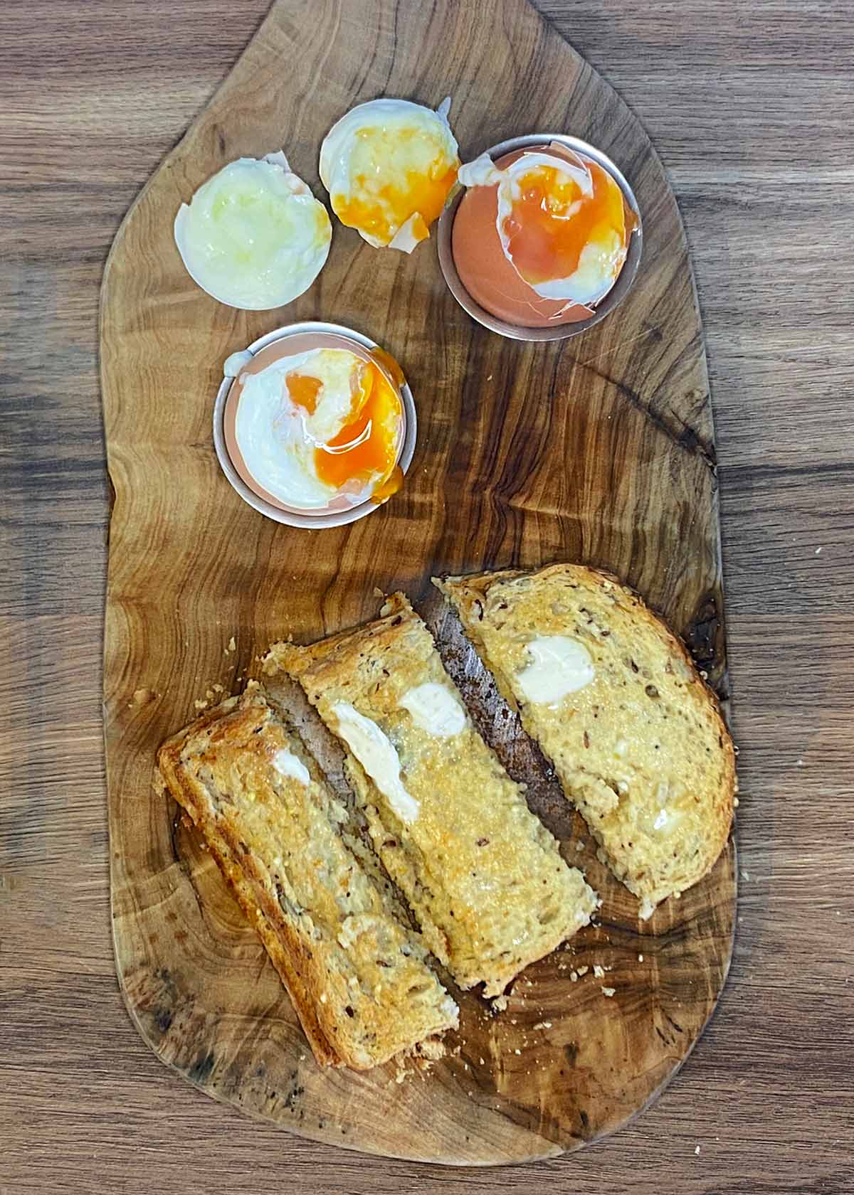 Two soft boiled eggs with the tops removed next to some sliced toast.