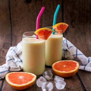 Two glasses of grapefruit smoothie next to slices of grapefruit.