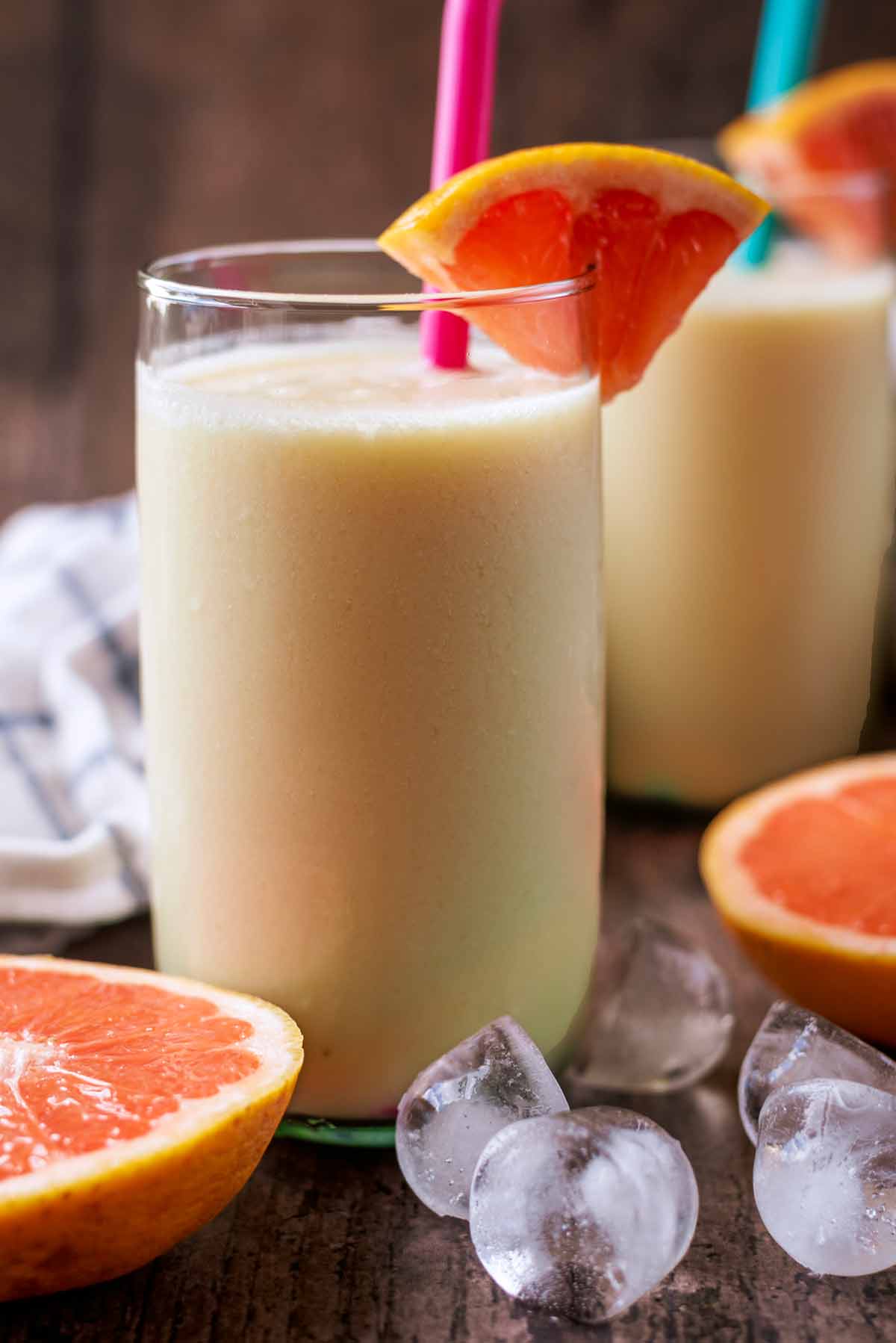 A smoothie in a tall glass with a wedge of grapefruit on the rim.