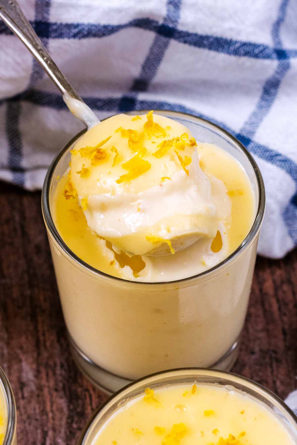 A spoon lifting some lemon posset out of a serving glass.