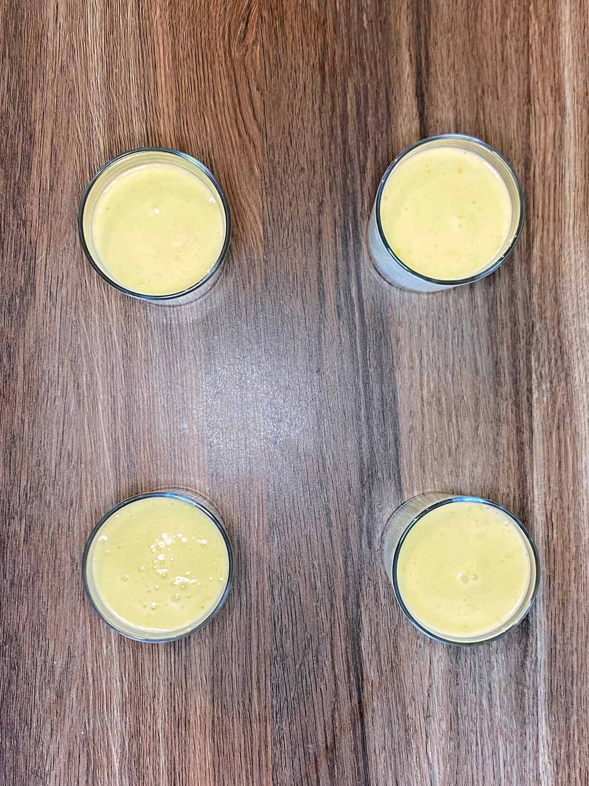 Four serving glasses containing unset lemon posset.