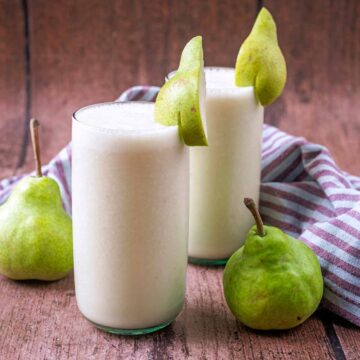 Two glasses of pear smoothie topped with slices of pear.