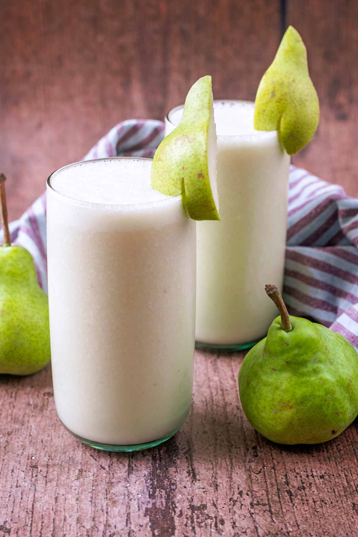 Two glasses of cream coloured smoothie next to two whole pears.