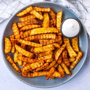 Peri peri fries on a plate with a small pot of mayonnaise.