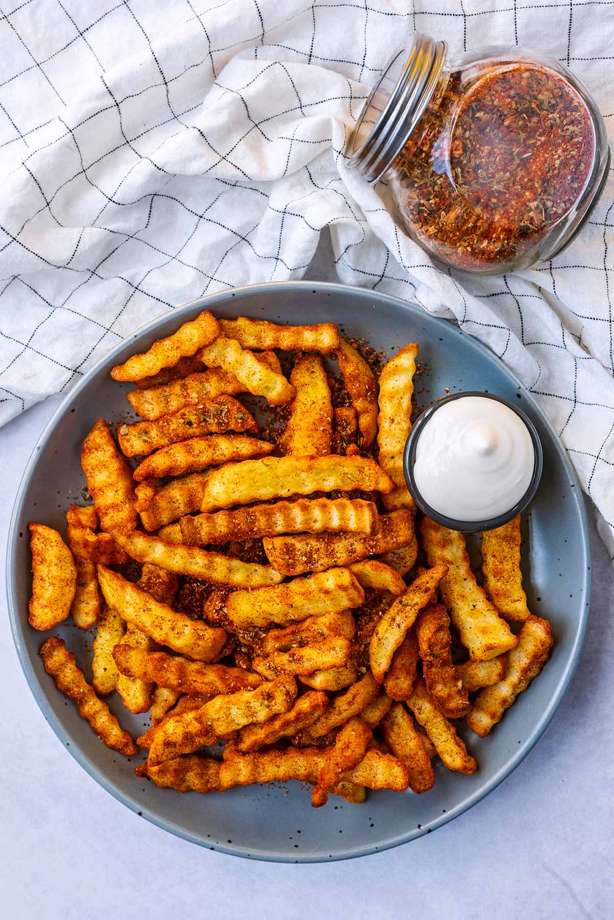A plate of seasoned chips next to a towel and a jar of seasoning.