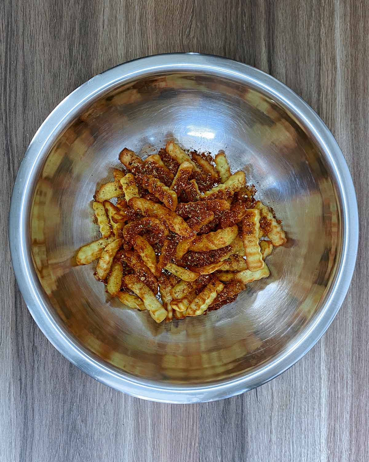 Cooked chips coated in seasoning in a metal bowl.