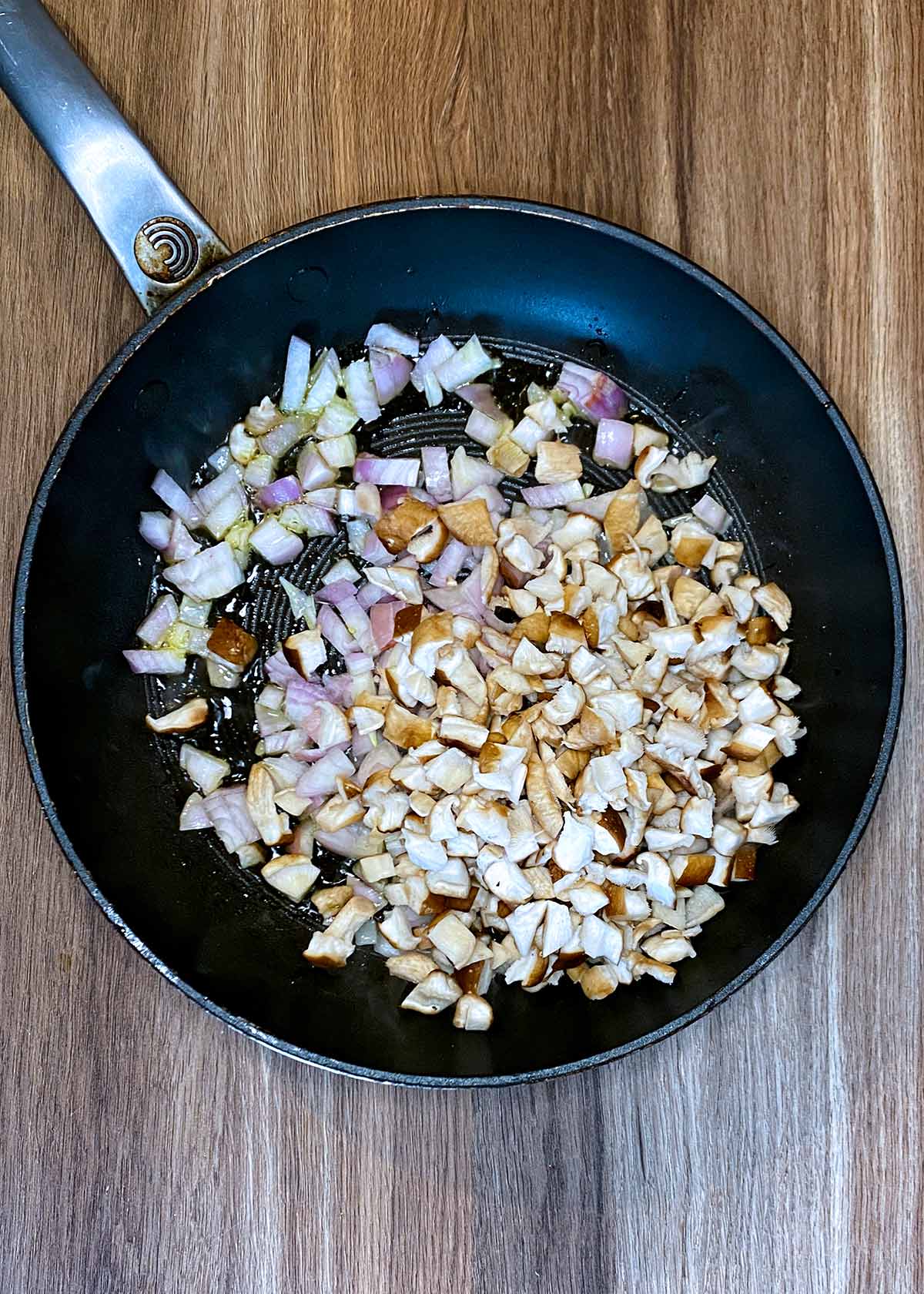 A frying pan with diced mushrooms and shallots cooking in it.