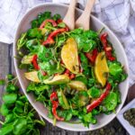 A bowl of watercress salad with a wooden fork and spoon in it.