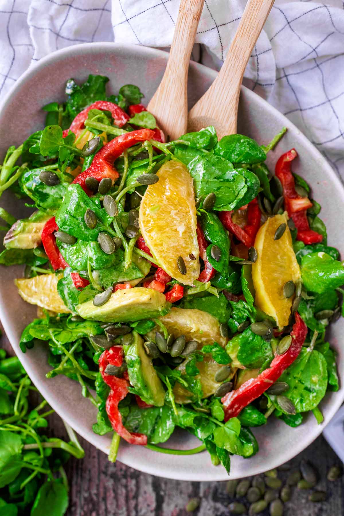 A salad of green leaves, red pepper, orange and avocado.